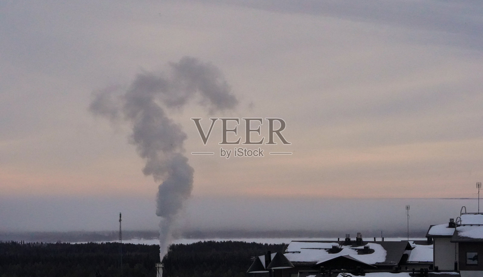 工厂烟雾飘散在雪白的冬季风景上。照片摄影图片