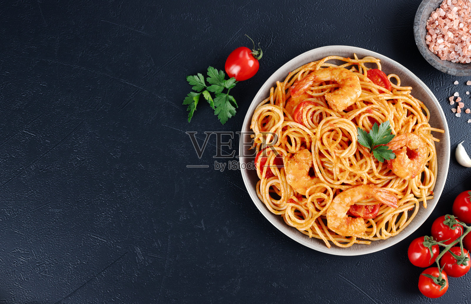 黑色背景上的意大利面条配虾和番茄酱。俯视图。留白。意大利美食。照片摄影图片