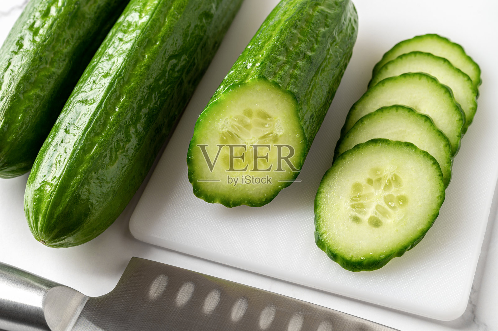 白色切菜板上的多汁黄瓜片和半根黄瓜。低卡路里的生蔬菜小吃。素食沙拉，有机蔬菜，丰收概念。照片摄影图片