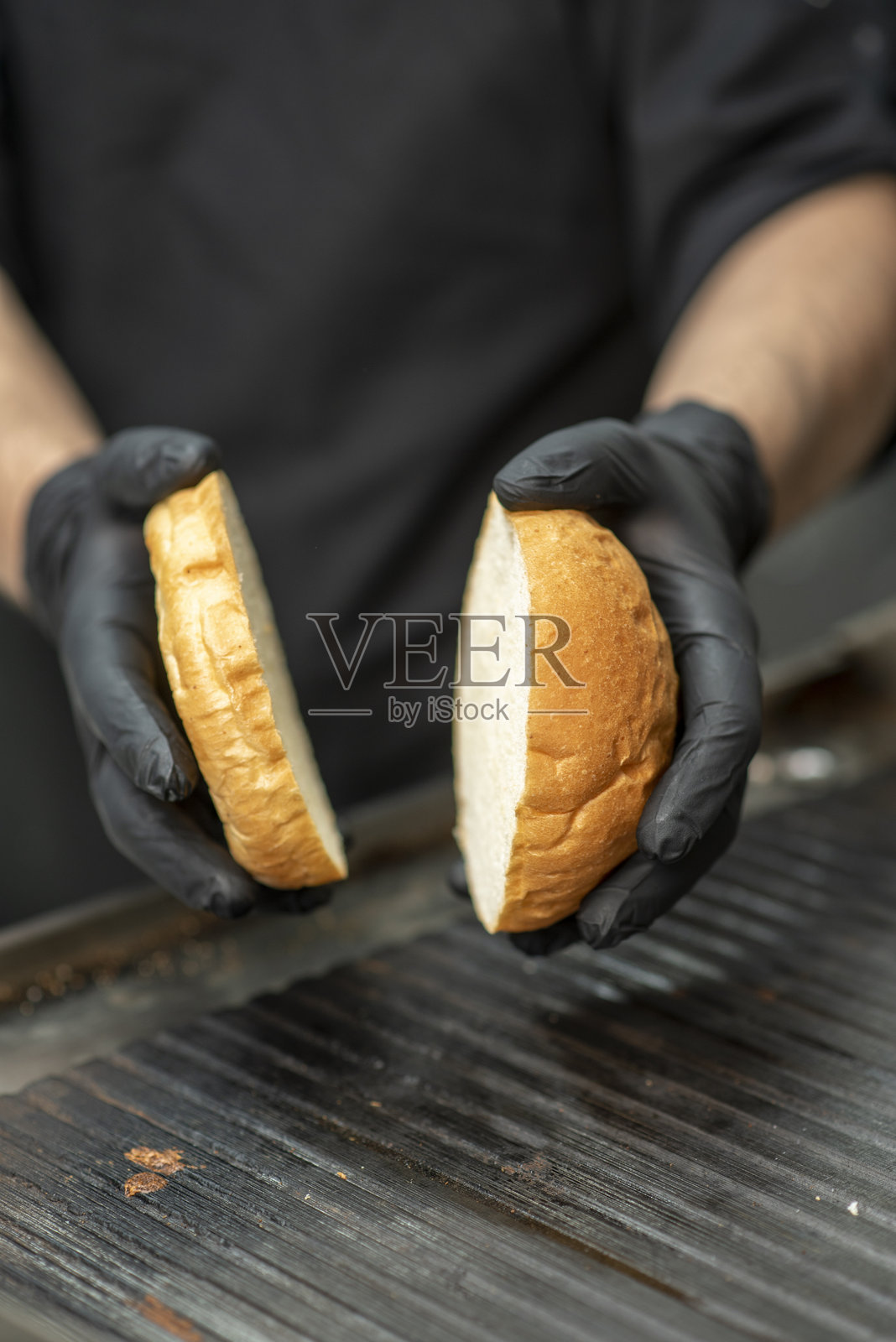 厨师戴着黑手套在快餐店准备美味汉堡，搭配新鲜蔬菜、酱汁和肉饼。照片摄影图片