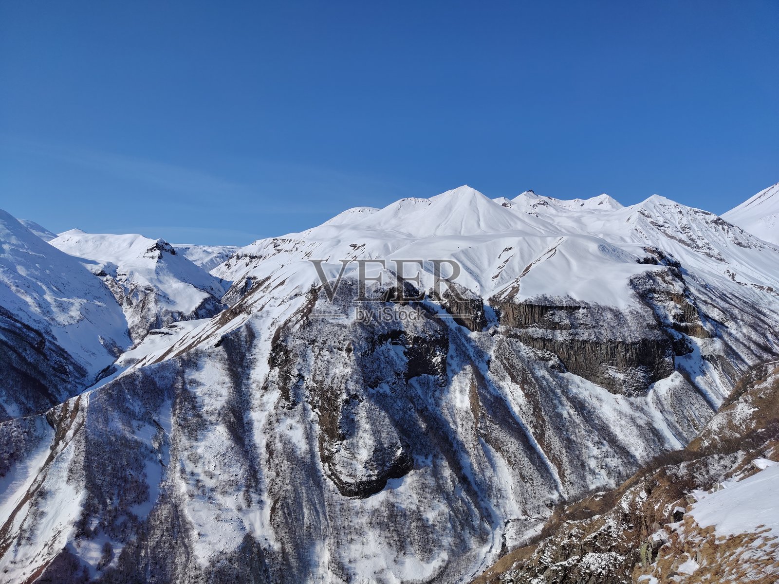 从格鲁吉亚军事公路的俄罗斯-格鲁吉亚友谊纪念碑俯瞰高加索山脉的雪山和蓝天的美丽景色照片摄影图片