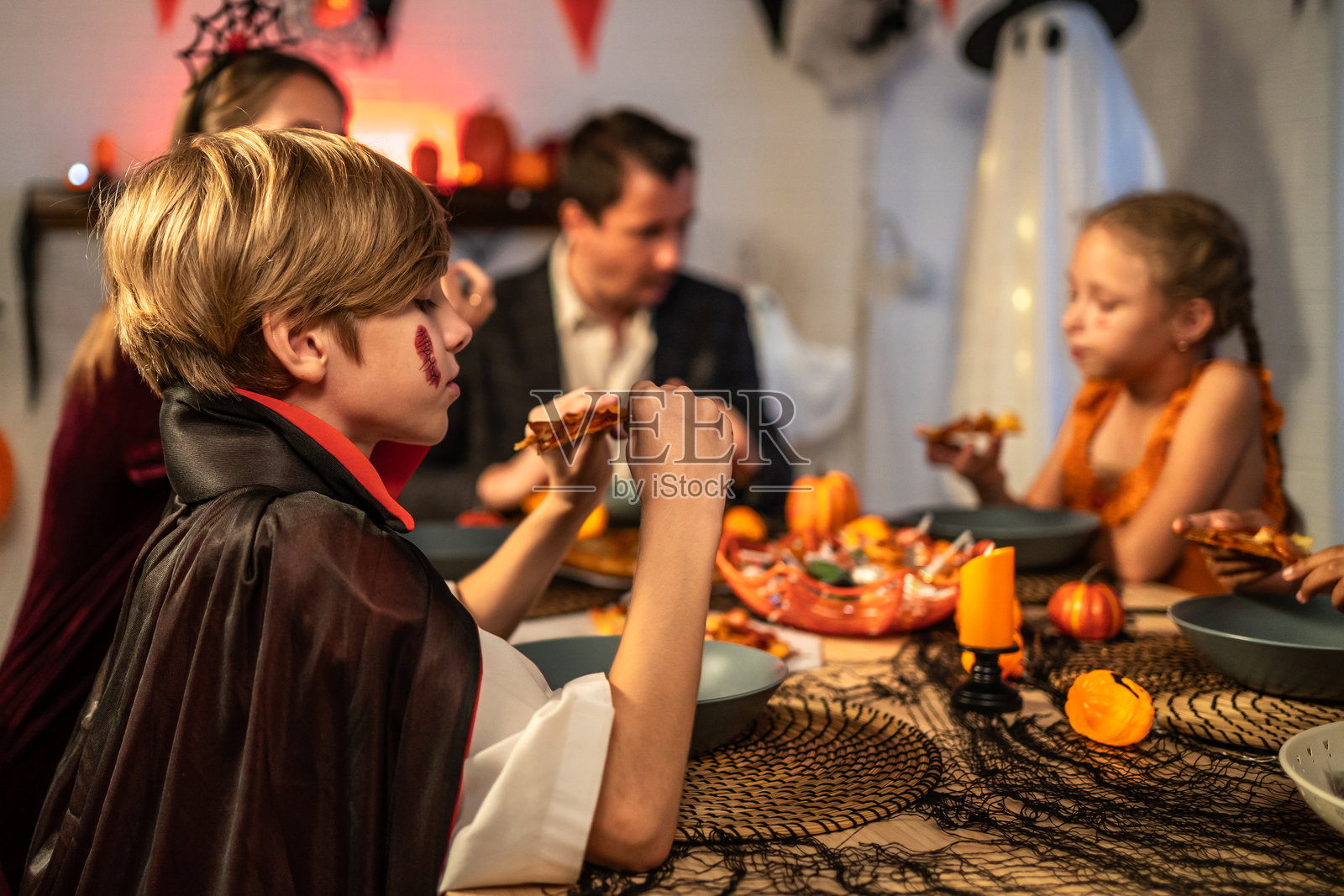 白人家庭在家中一起庆祝万圣节派对。迷人的父母和孩子们穿着万圣节服装，享用晚餐，庆祝节日。照片摄影图片
