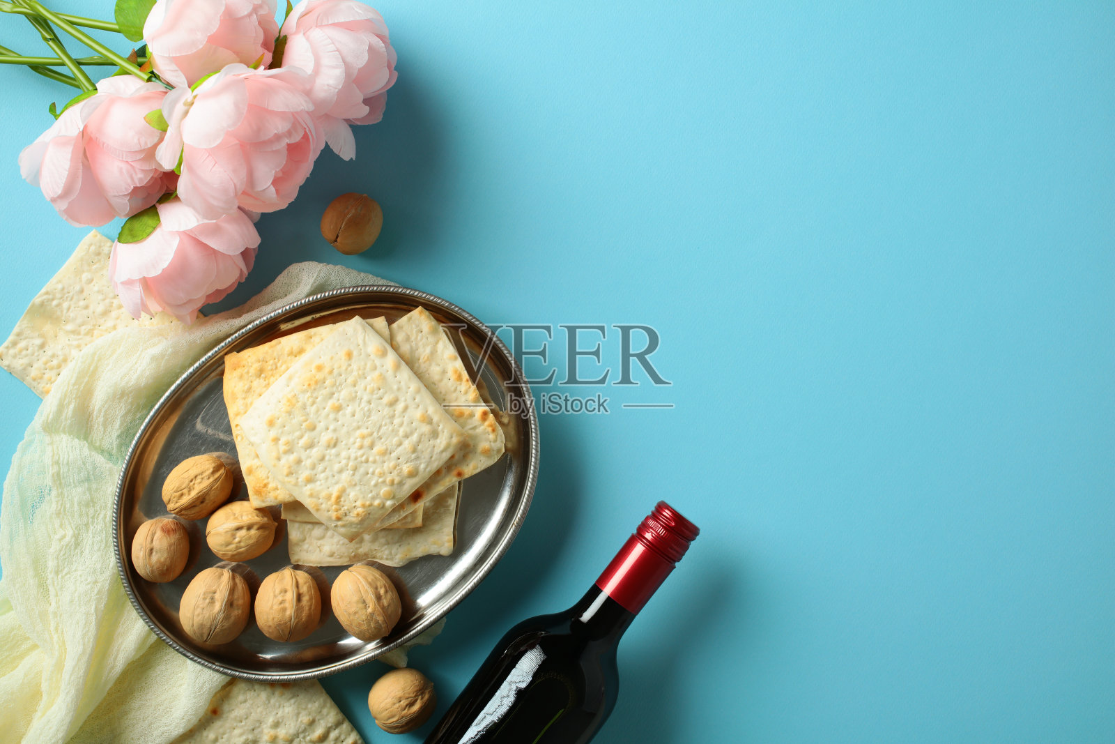 逾越节，犹太节日佩萨赫的概念。优雅的静物画，背景为蓝色，包含粉色花朵、无酵饼、核桃和红酒。照片摄影图片