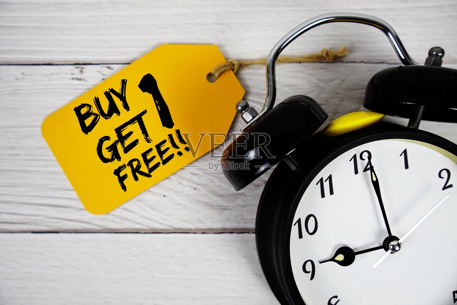 价格标签上的“买一送一”文字，背景为木质的闹钟。照片摄影图片