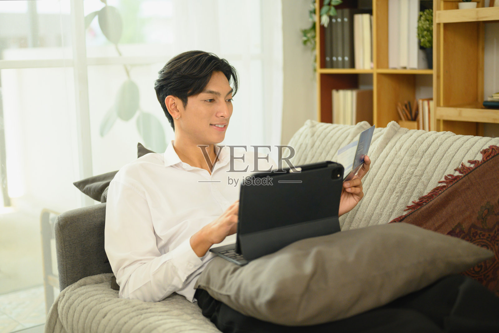 微笑的亚洲男子手持存折，正在数字平板上查看财务交易照片摄影图片