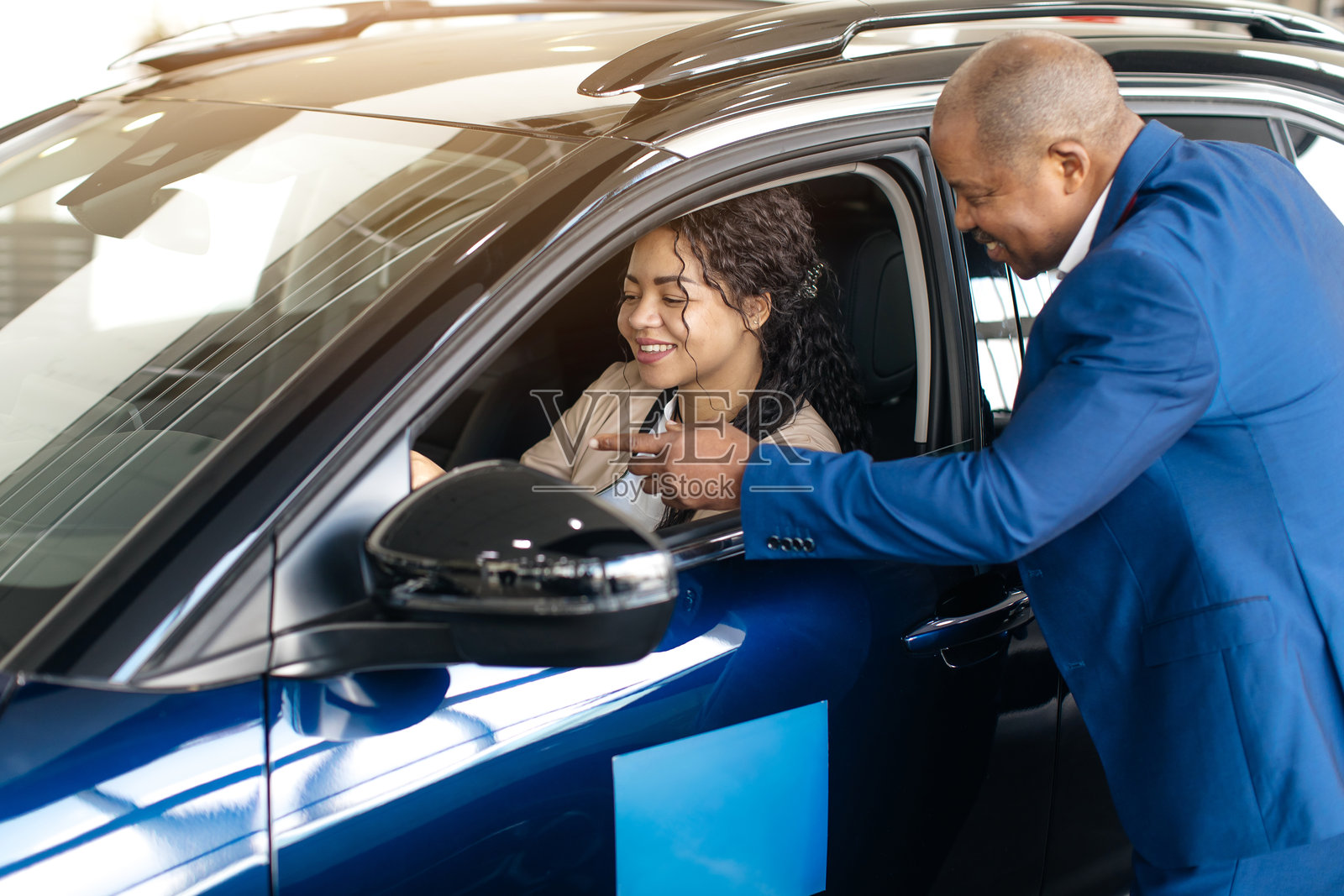 快乐的非洲女性在汽车经销商展厅购买新车，测试并与销售员交谈。女性正在选择汽车。照片摄影图片