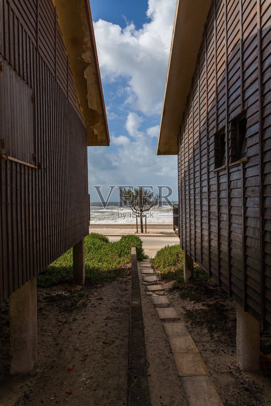 两座带红瓦屋顶的乡村木屋并排而立，位于明亮的部分多云天空下，展示了简单的乡村建筑风格。照片摄影图片