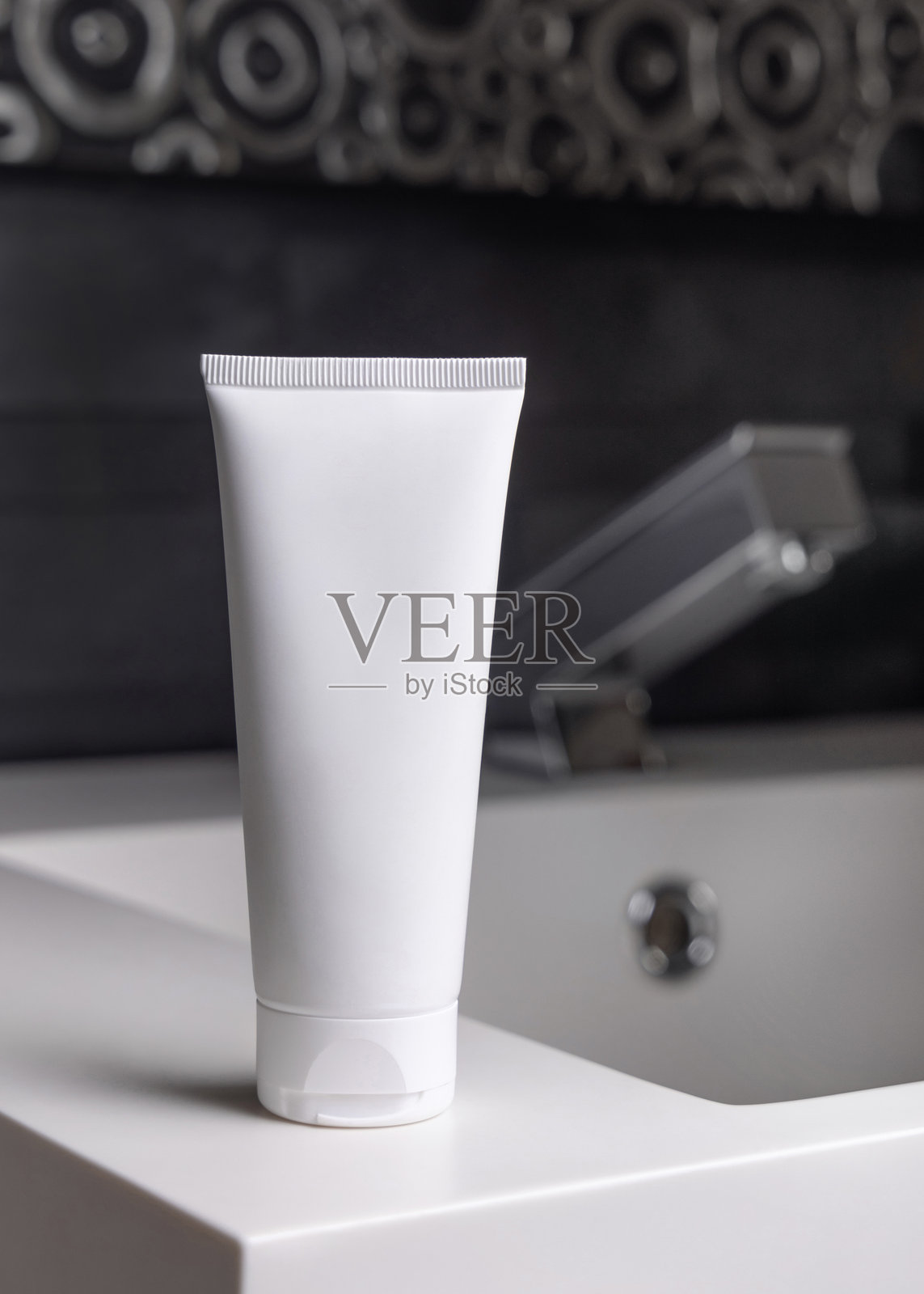 深灰色浴室中，现代水龙头旁的白色护肤霜管，特写化妆品展示。照片摄影图片