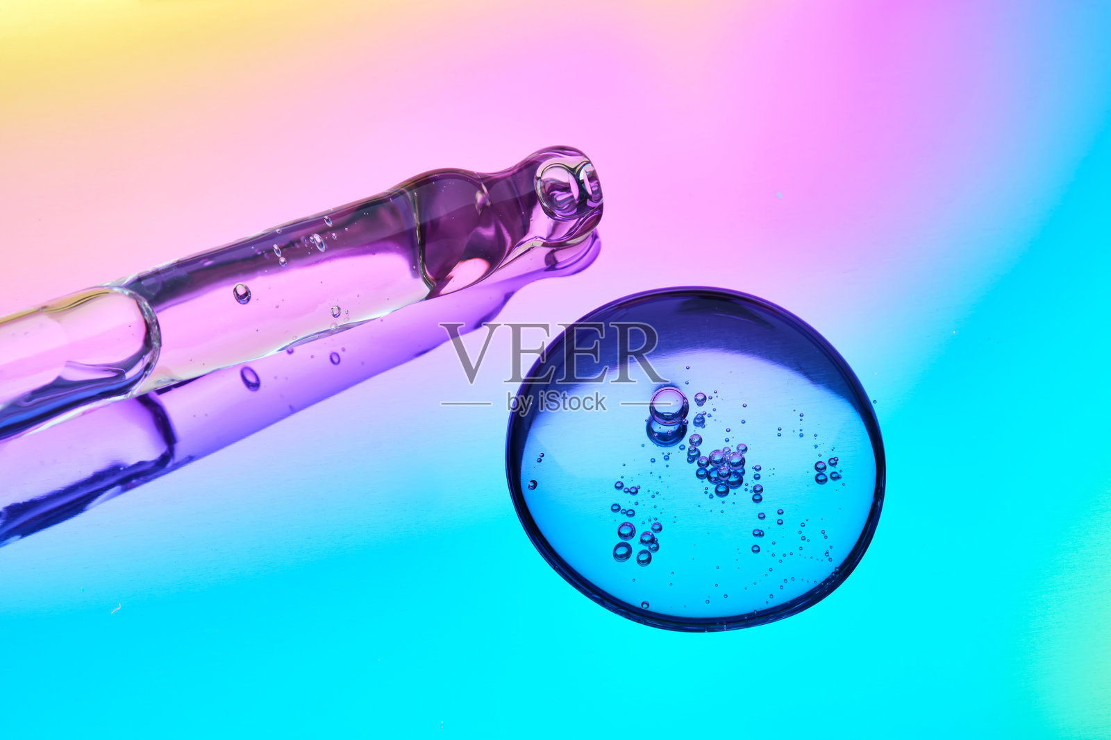 一滴化妆品精华和一个吸管置于蓝色和紫色渐变的多彩背景上。照片摄影图片