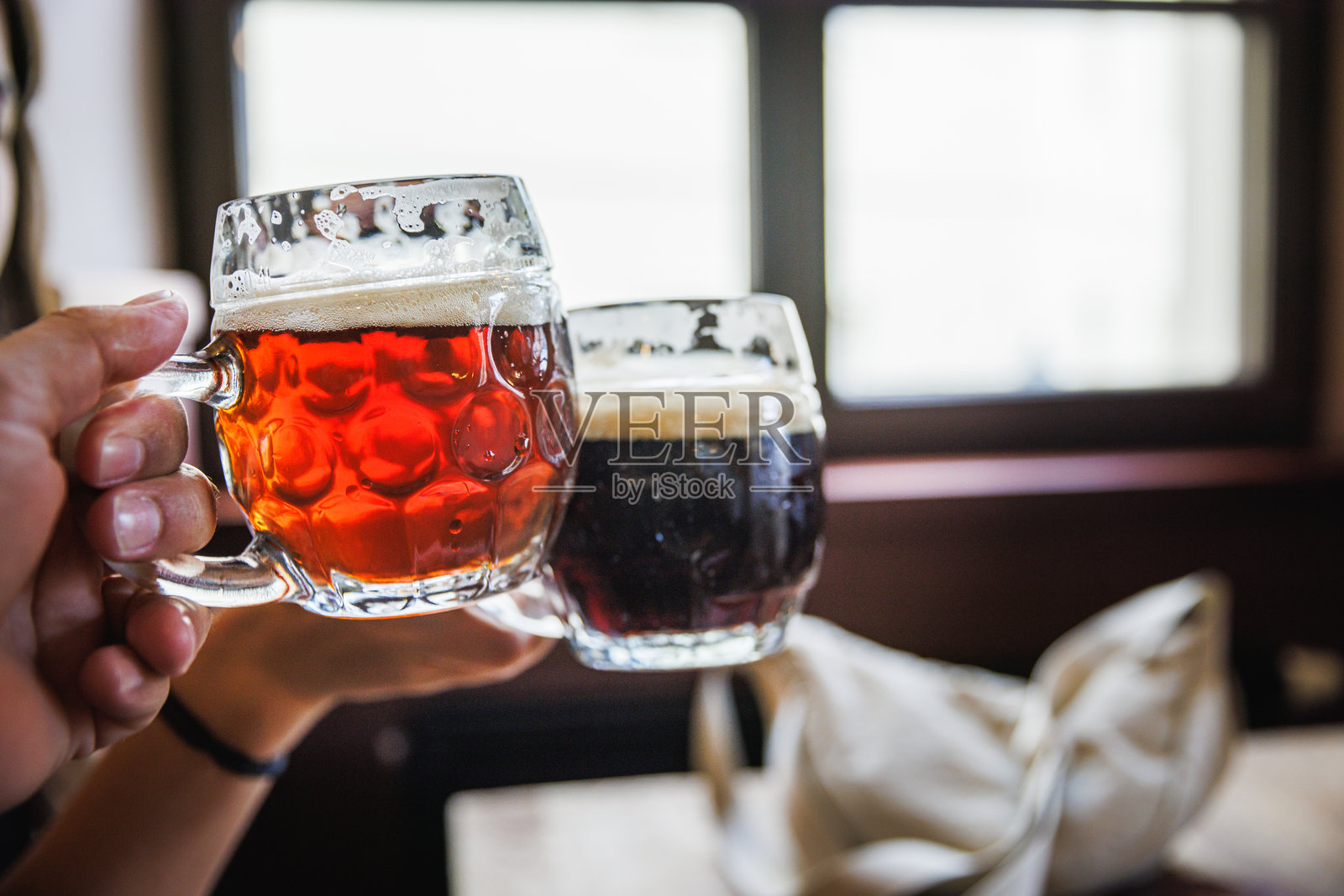 手持新鲜冷却的红色和深色啤酒玻璃杯照片摄影图片