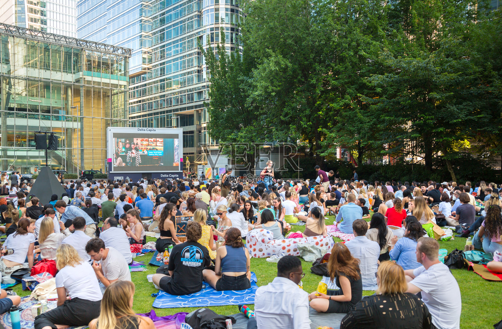 加拿大广场上人潮涌动，办公族在下班后享受公共活动。人们在金丝雀码头观看电影，喝饮料，享受野餐。照片摄影图片