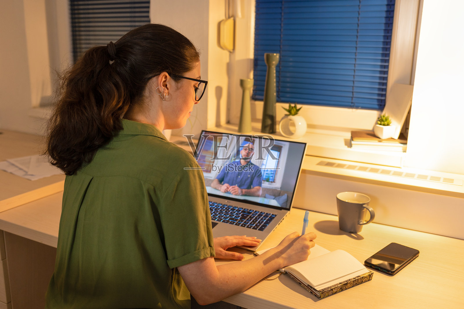 年轻女性在笔记本电脑前工作的背影。居家远程工作和在线通话。与心理学家的远程咨询。现代自由职业和教育的概念。照片摄影图片