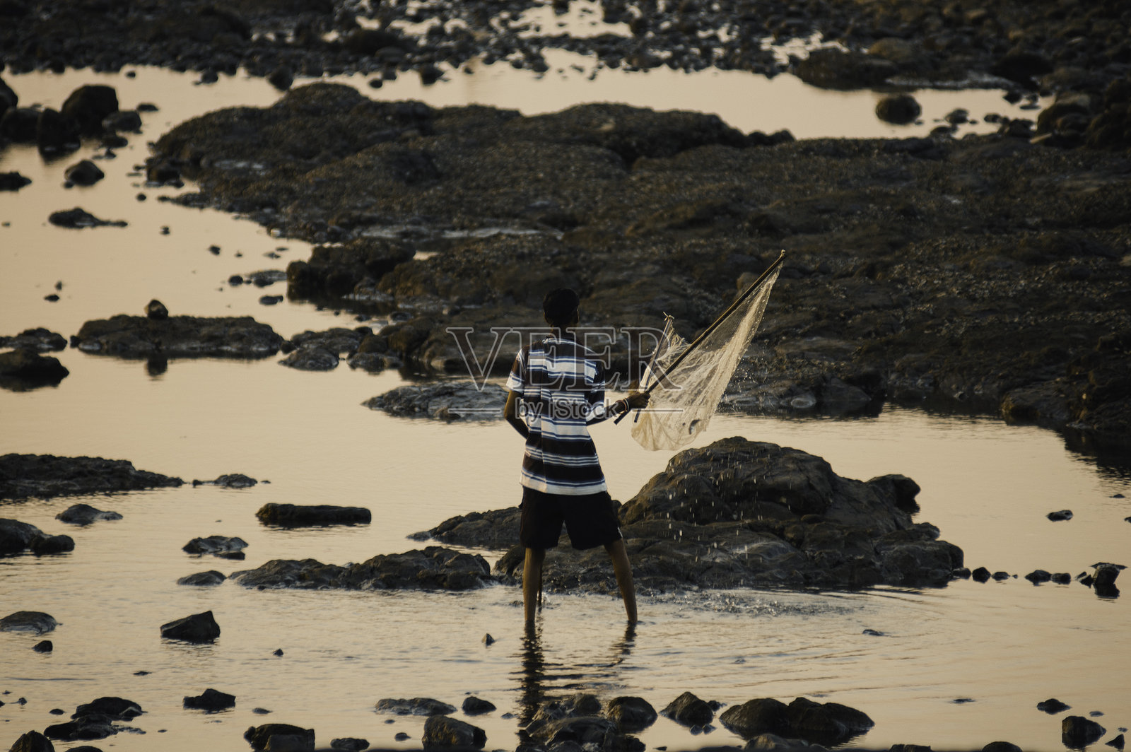 一位印度男子在日落时分的海岸线轮廓中垂钓照片摄影图片