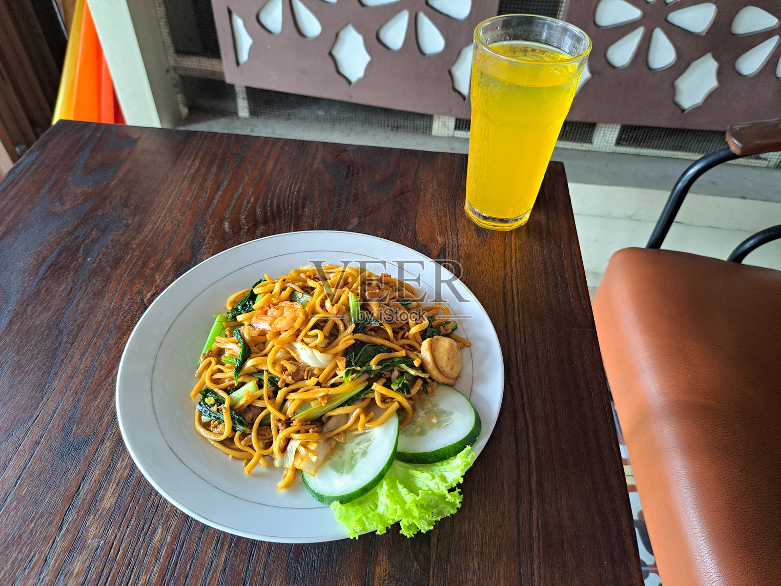 海鲜炒面配牛肉片、虾仁、蟹肉、炸洋葱、绿芥菜、黄瓜和生菜。新鲜橙汁装在玻璃杯中。食品和饮料菜单。照片摄影图片