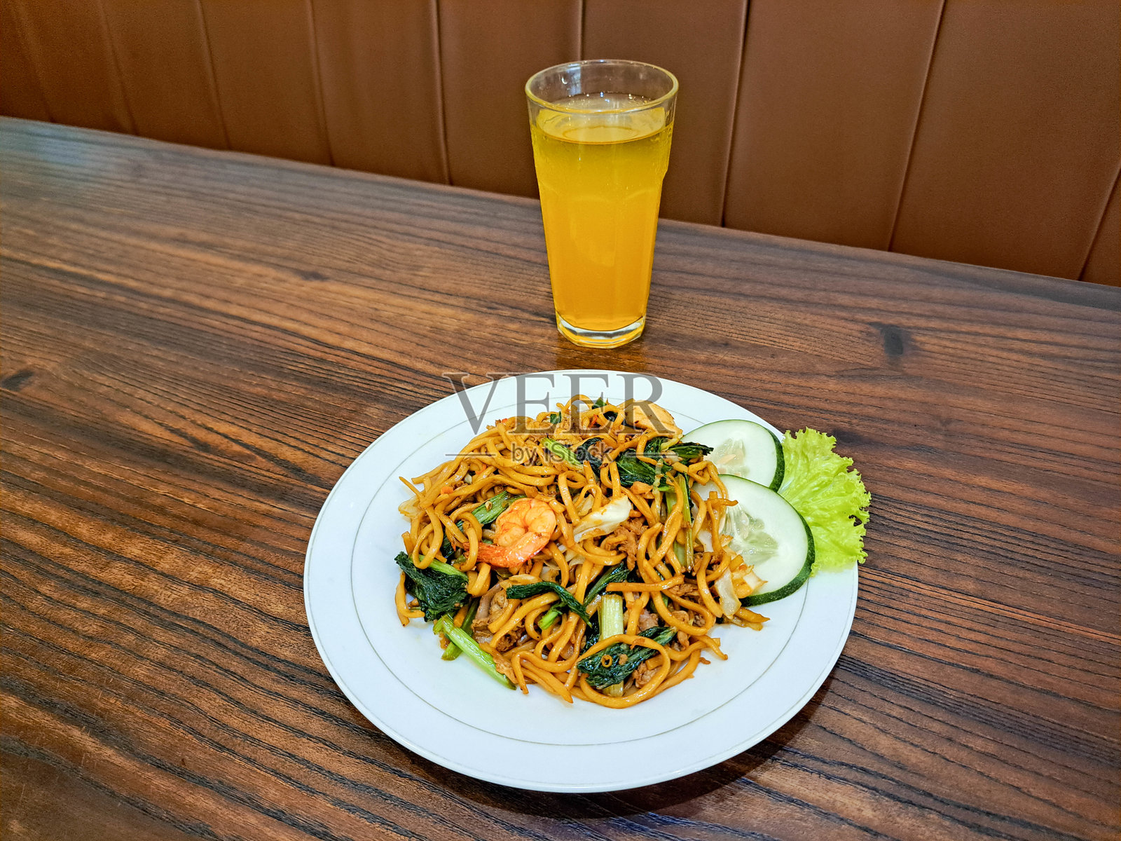 美味的海鲜炒米粉，配有牛肉片、虾仁、蟹肉、炸洋葱、青芥菜、黄瓜和生菜。新鲜的橙汁装在玻璃杯中。食品和饮料菜单。照片摄影图片