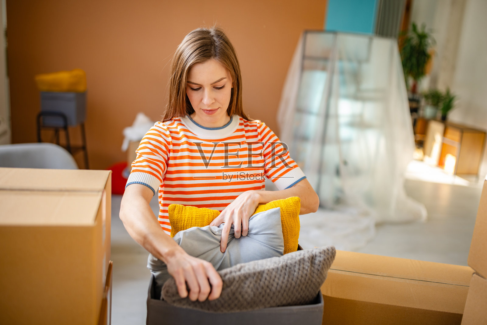 年轻女性在新公寓中拆包舒适的枕头，享受她激动人心的搬家旅程照片摄影图片