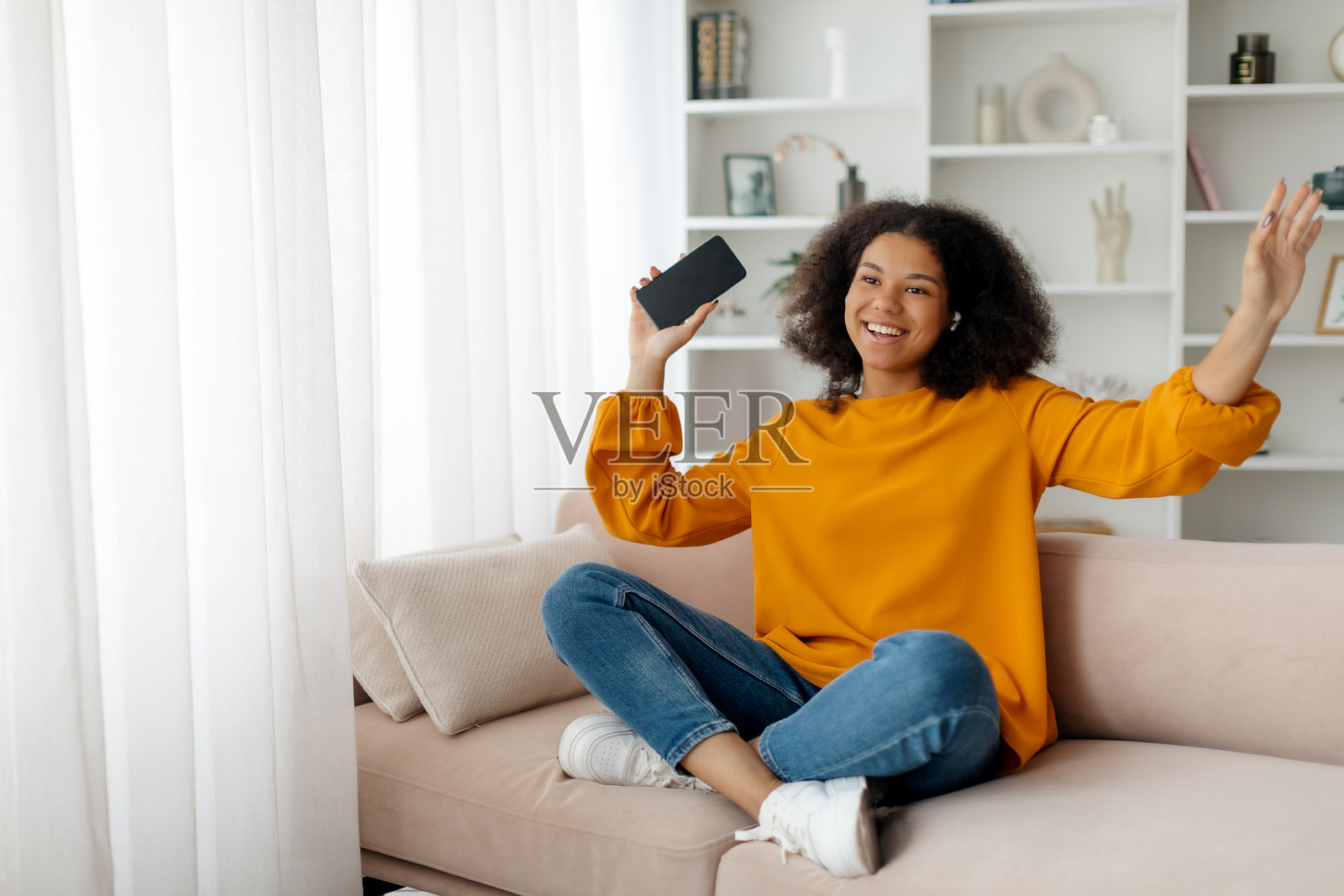 最爱的休闲时光。快乐的非洲女士在家中一边听音乐一边唱歌，快乐的非裔美国女性戴着无线耳机，在客厅的沙发上享受乐趣。照片摄影图片