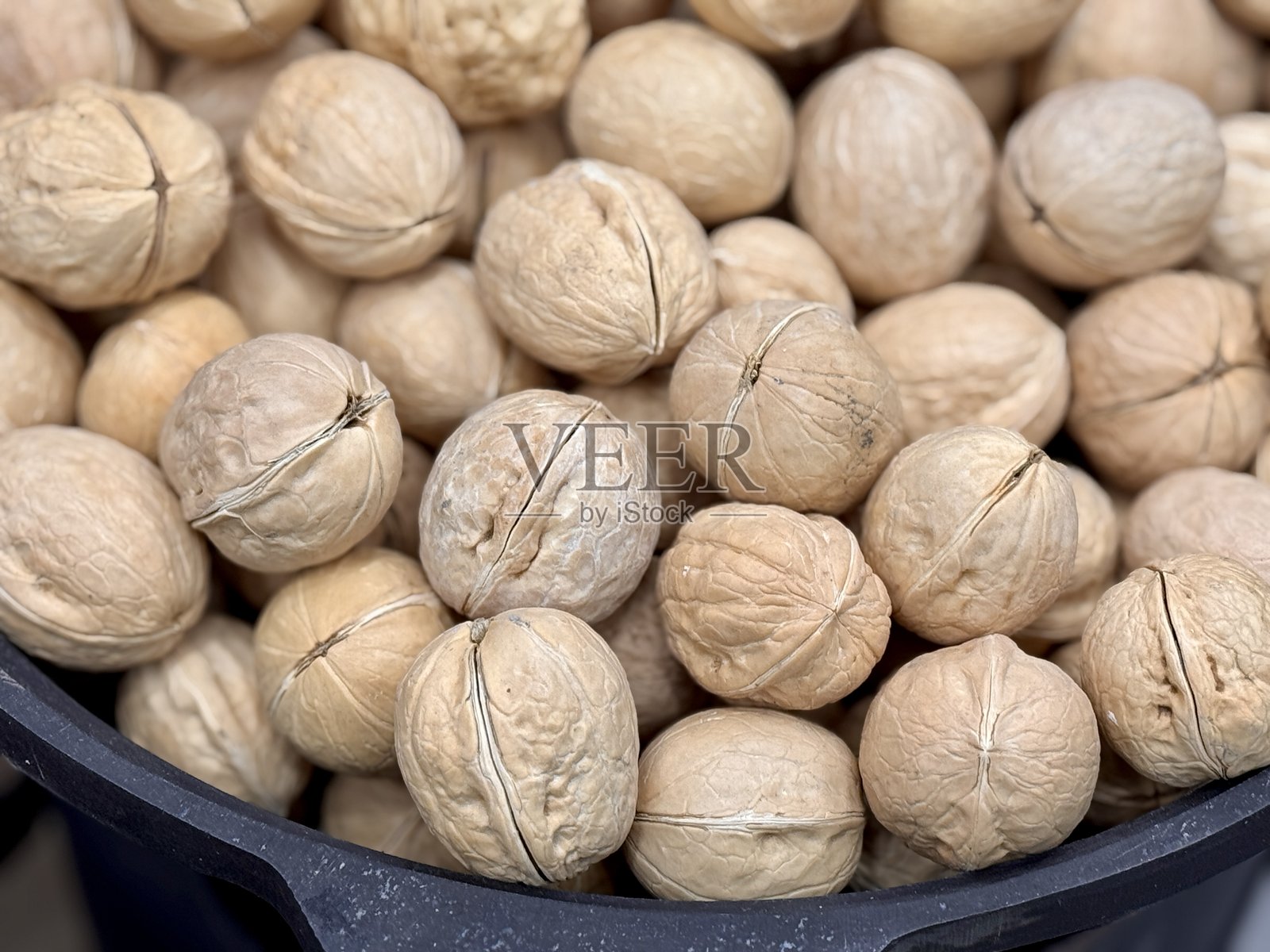 市场上黑色锅中大量整颗核桃出售。健康饮食。特写。照片摄影图片