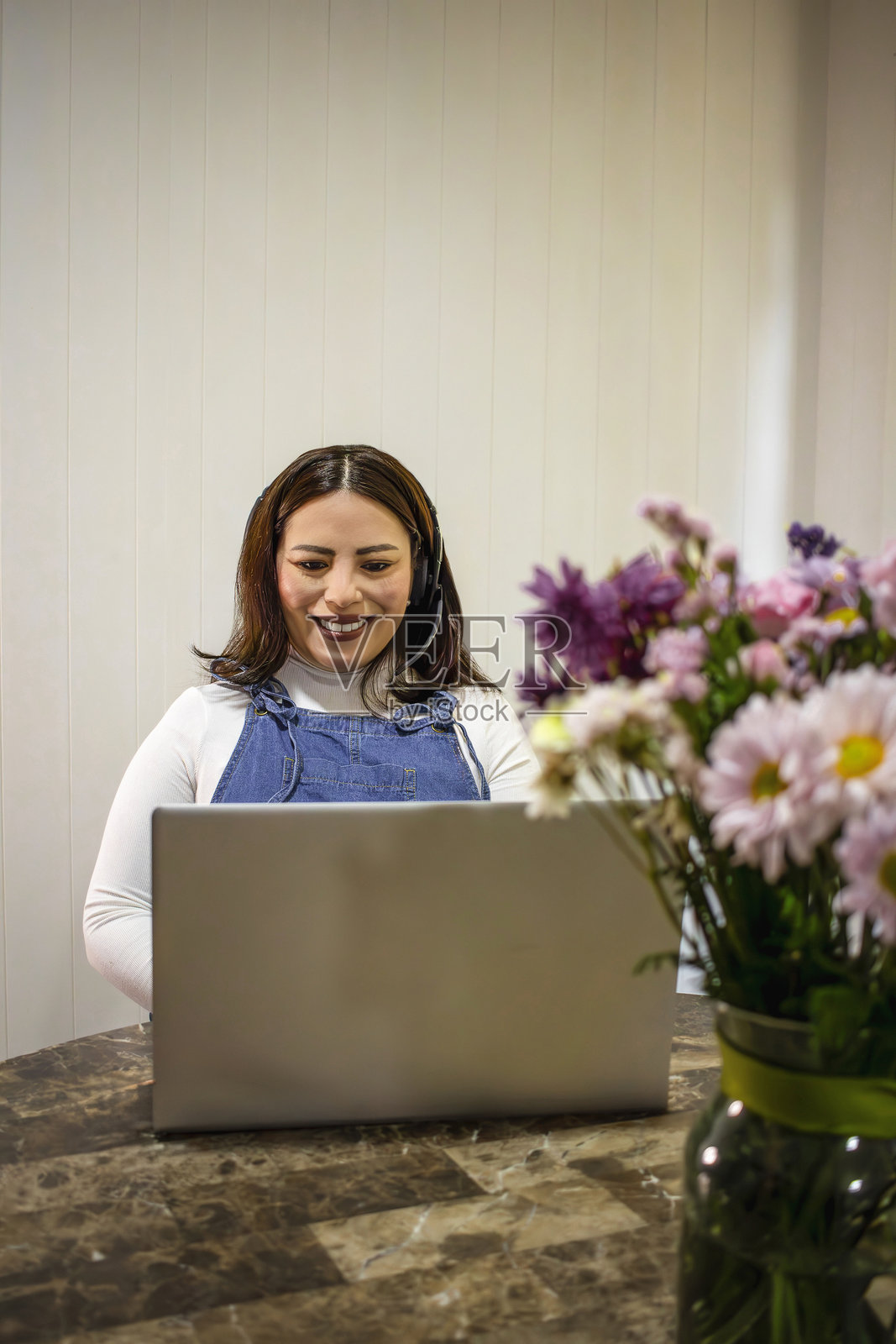 戴着耳机的女性在远程工作，使用笔记本电脑照片摄影图片