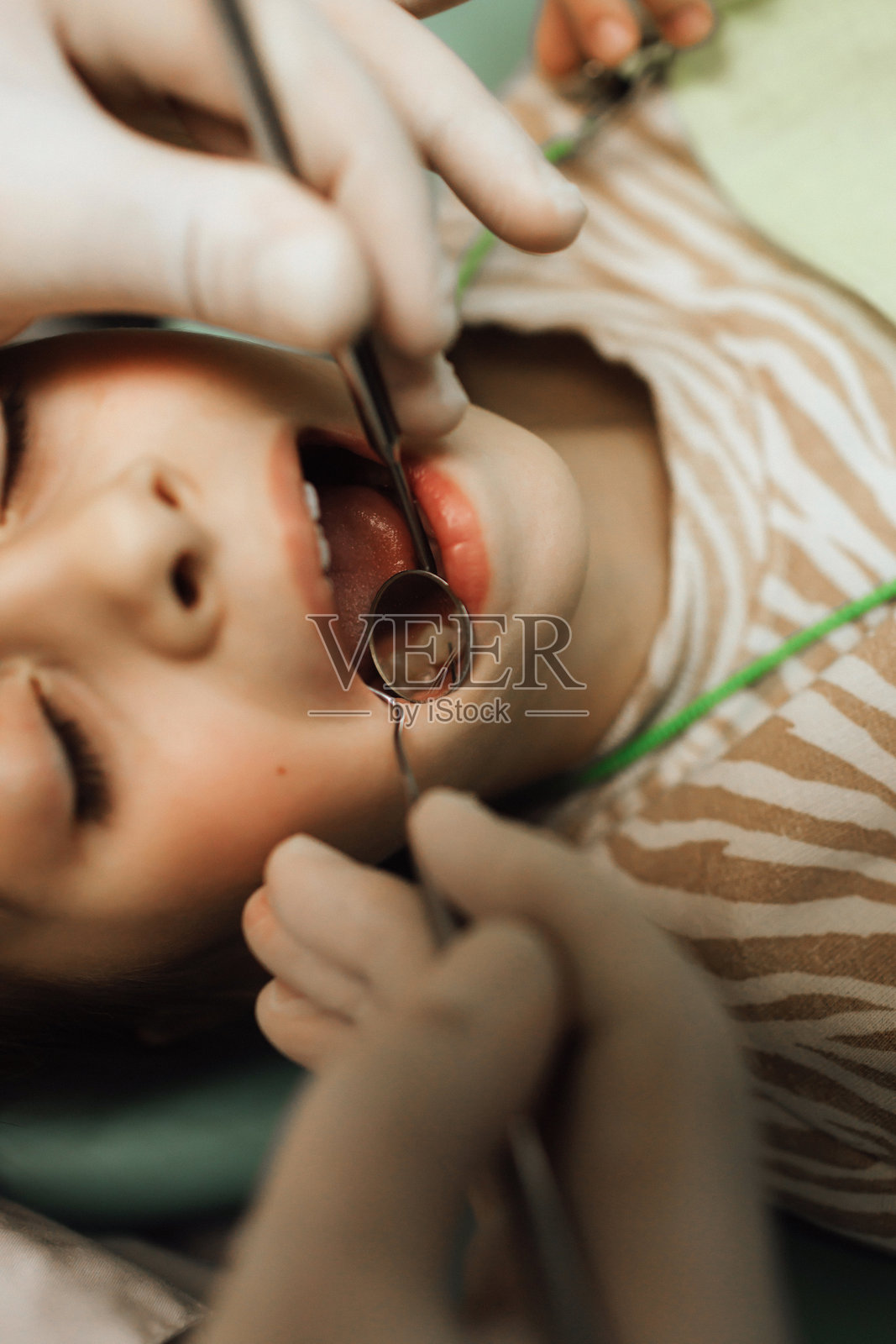 坐在牙科椅上的小女孩，扎着辫子，正看着镜头。一位戴着手套的医生手持检查工具。儿童牙科。系列的一部分。照片摄影图片