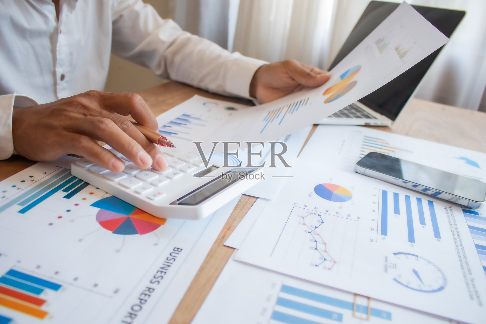 一名男子的手在笔记本电脑和手机上打字，同时查看投资文件，并使用计算器和电脑进行分析以降低风险。照片摄影图片