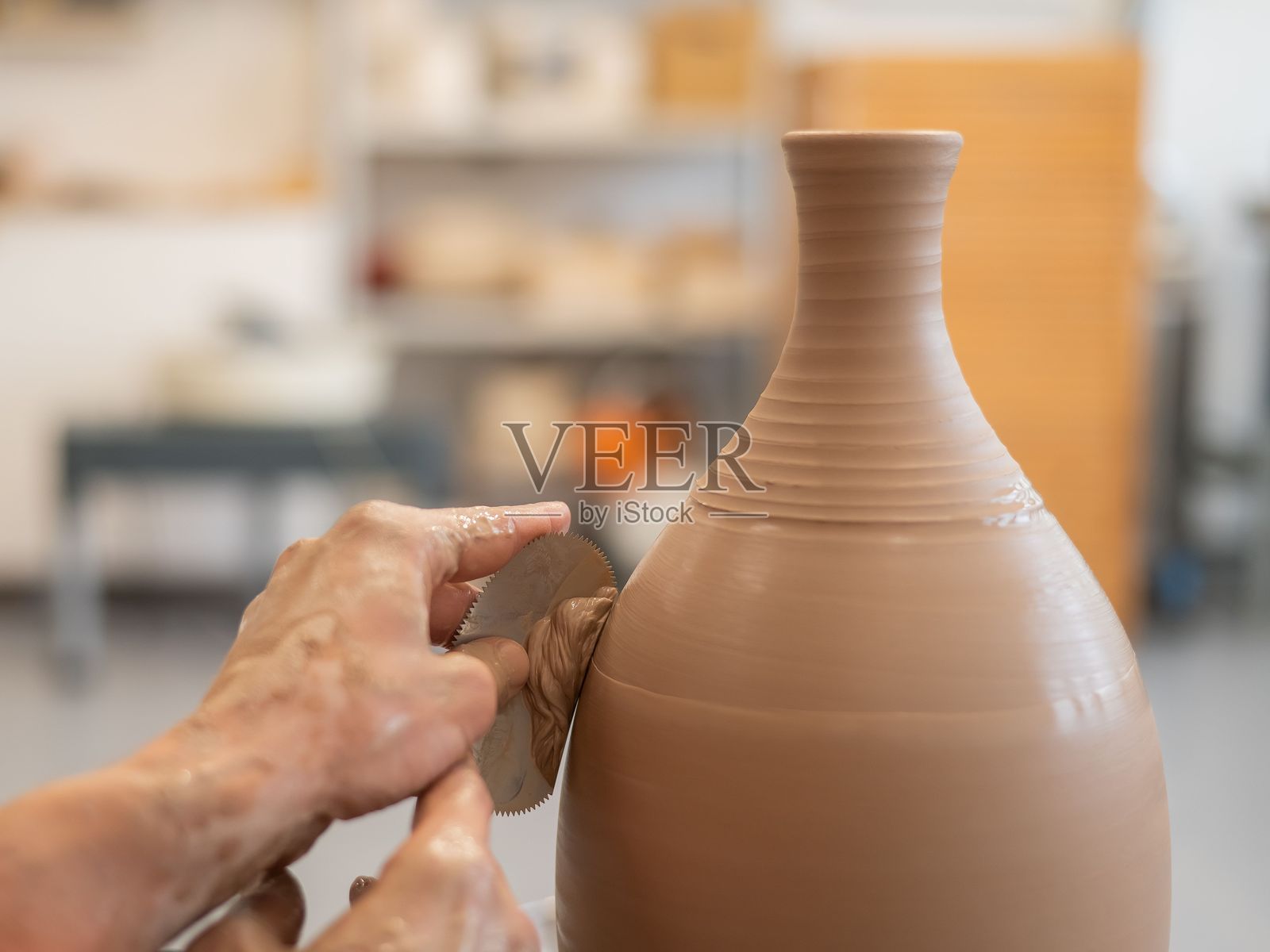 一位陶艺师在陶轮上使用工具修整花瓶的表面。照片摄影图片