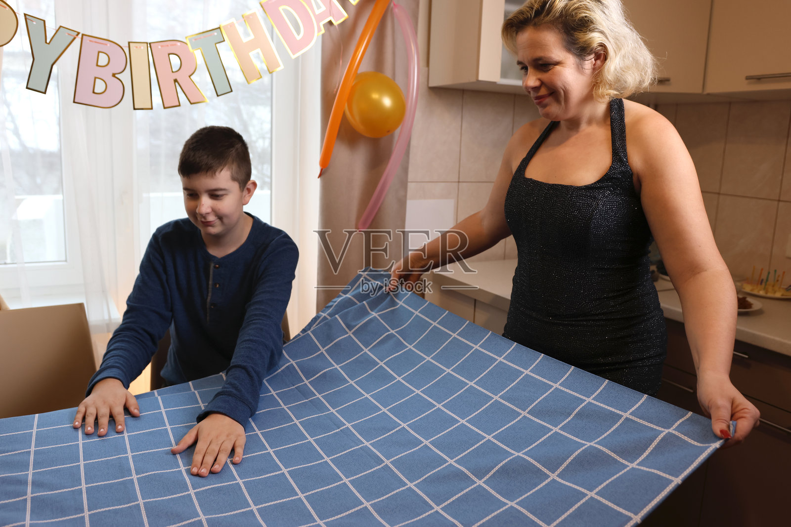 一位母亲与她的儿子和侄子一起为生日庆祝活动装饰房间和节日餐桌。柔和的灯光。照片摄影图片