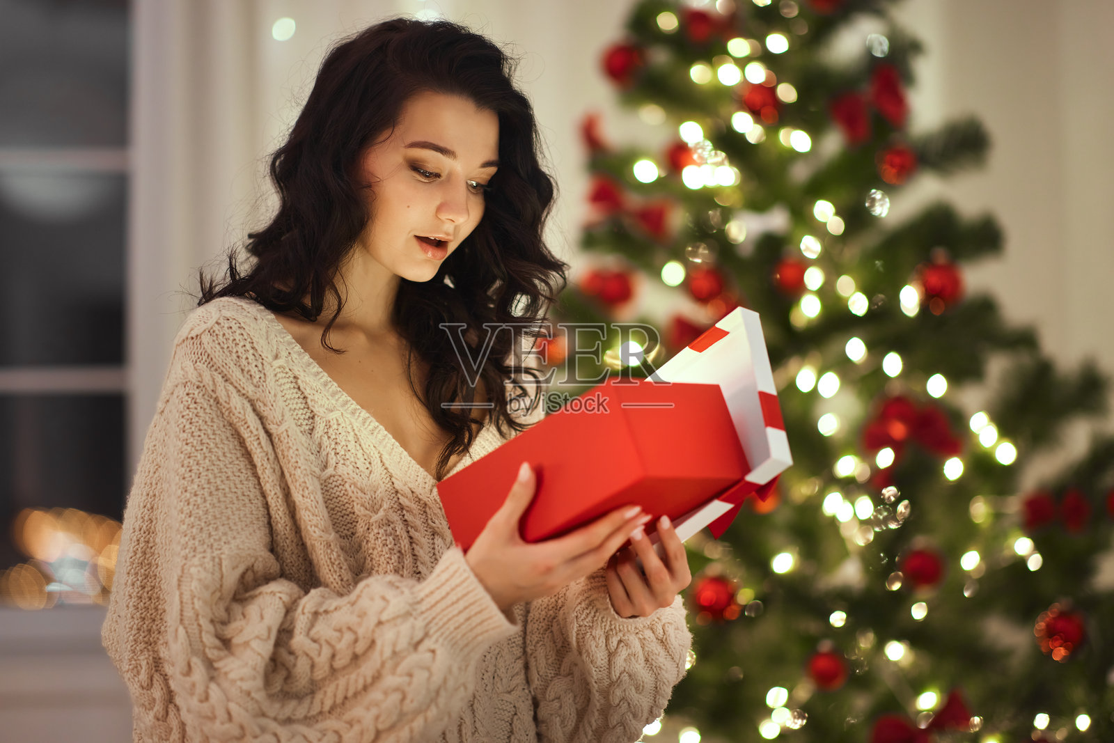 穿着舒适毛衣的女人在树旁拆圣诞礼物照片摄影图片