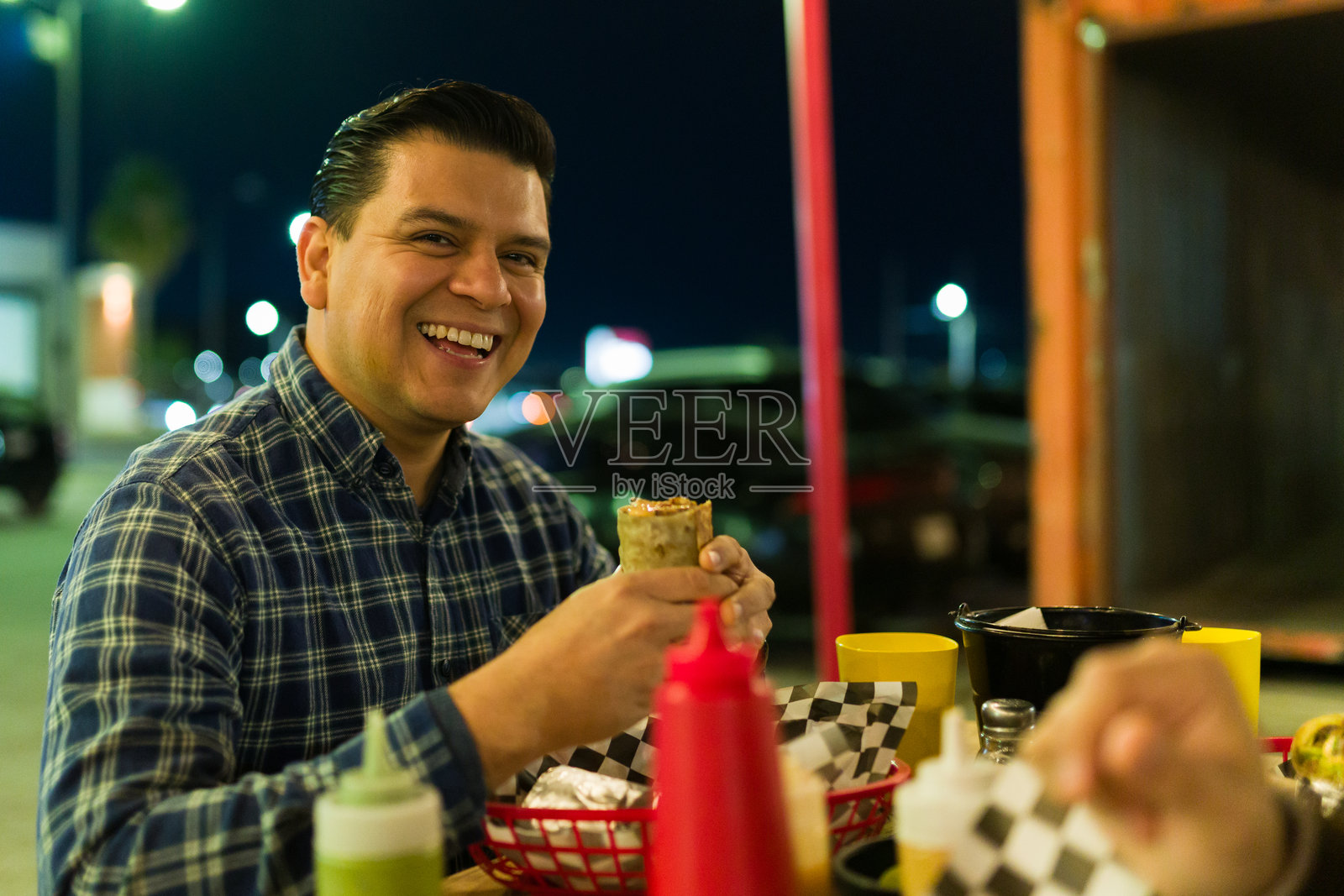快乐的男人在户外餐车享用美味的墨西哥卷饼，感受着热闹的夜生活照片摄影图片