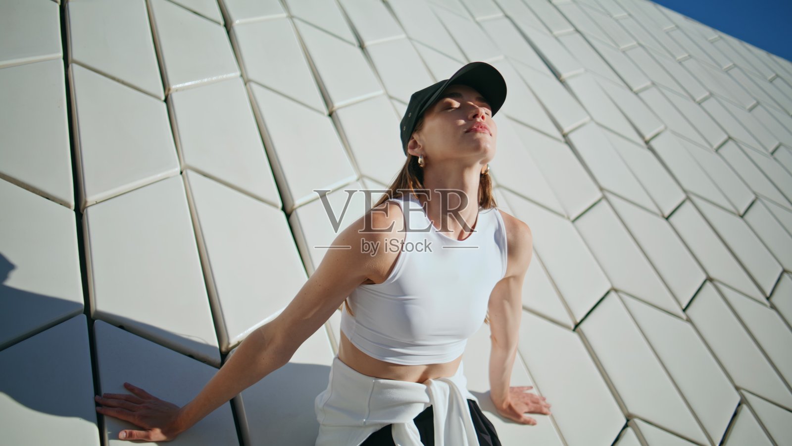 运动女性靠在现代纹理建筑的墙上，感受宁静，特写镜头。照片摄影图片