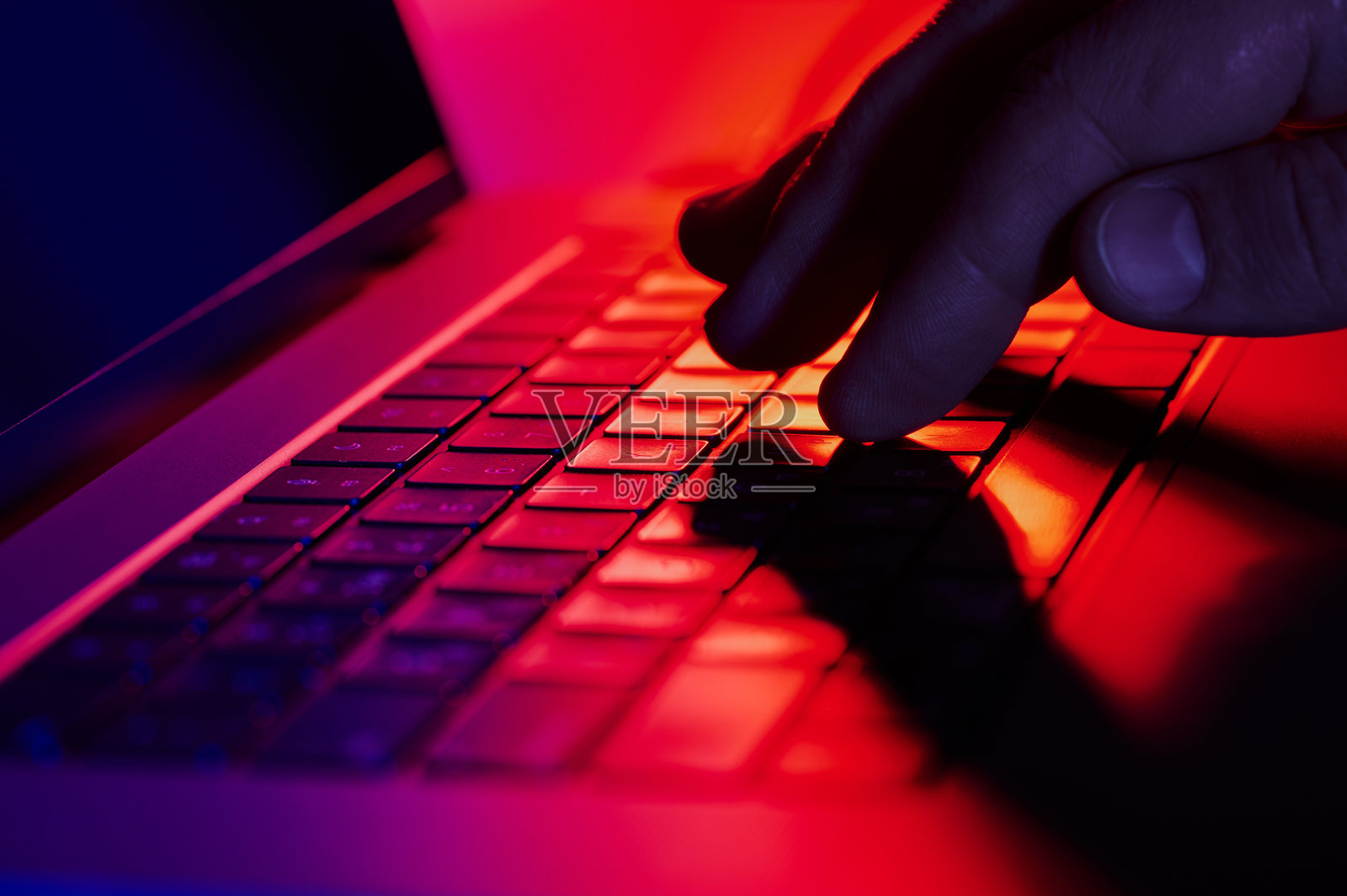 在黑暗环境中，手指在笔记本电脑键盘上打字，周围被鲜艳的彩色灯光照亮。照片摄影图片