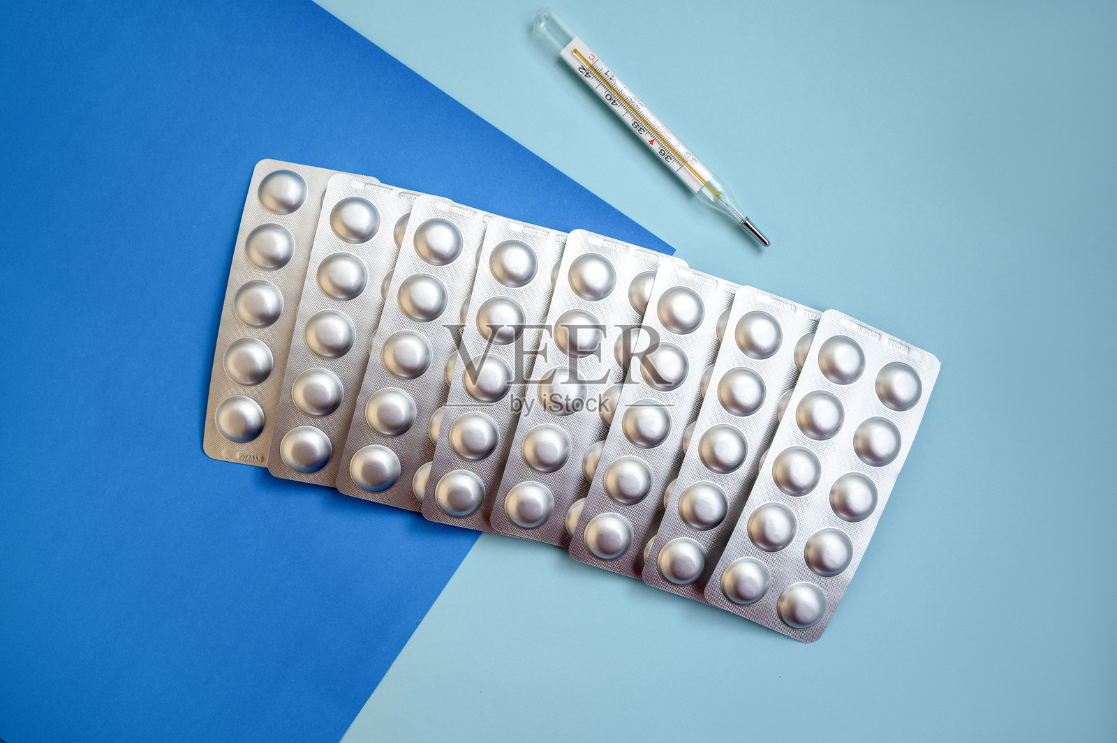 银色泡罩中的药片和蓝色背景上的温度计。照片摄影图片