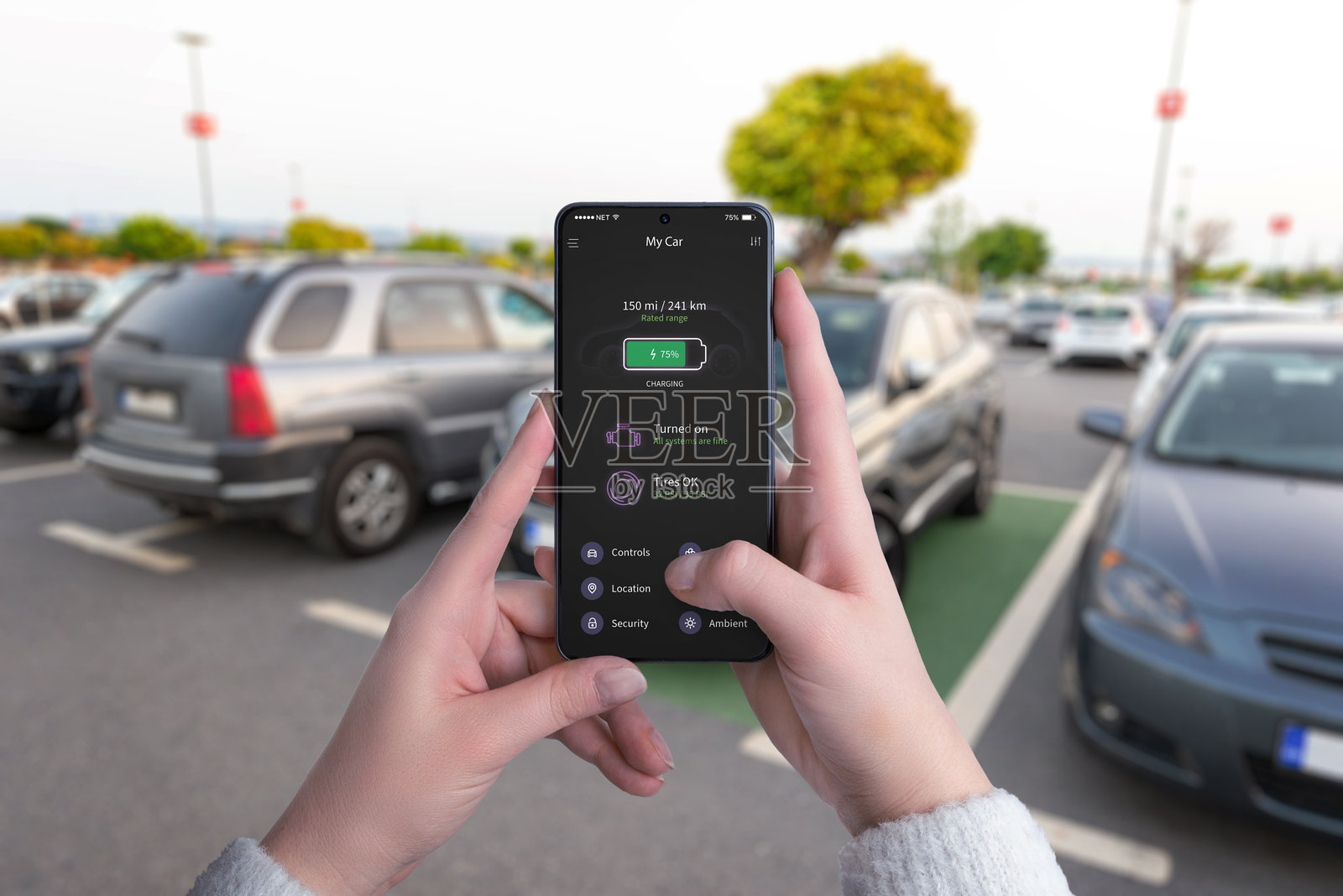 年轻女性在智能手机上查看“My Car”应用，监控现代停车场电动车充电站的充电状态。照片摄影图片