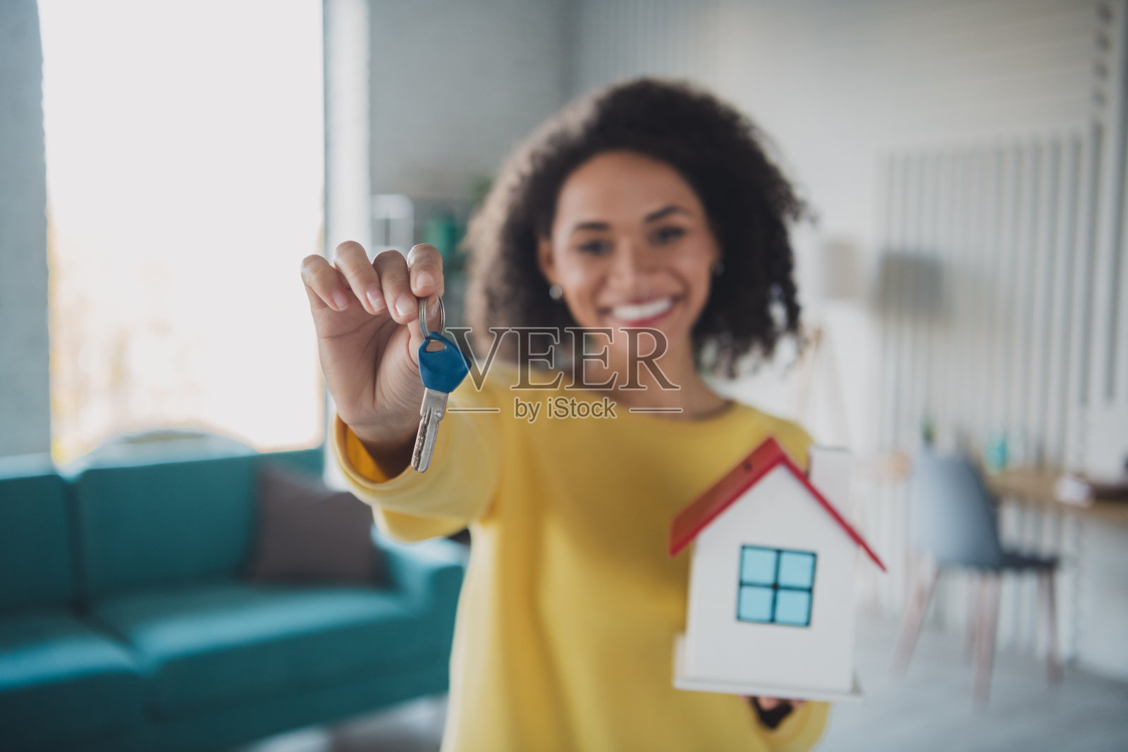快乐的年轻女性手握房屋钥匙和迷你模型，象征着拥有房屋的喜悦。照片摄影图片