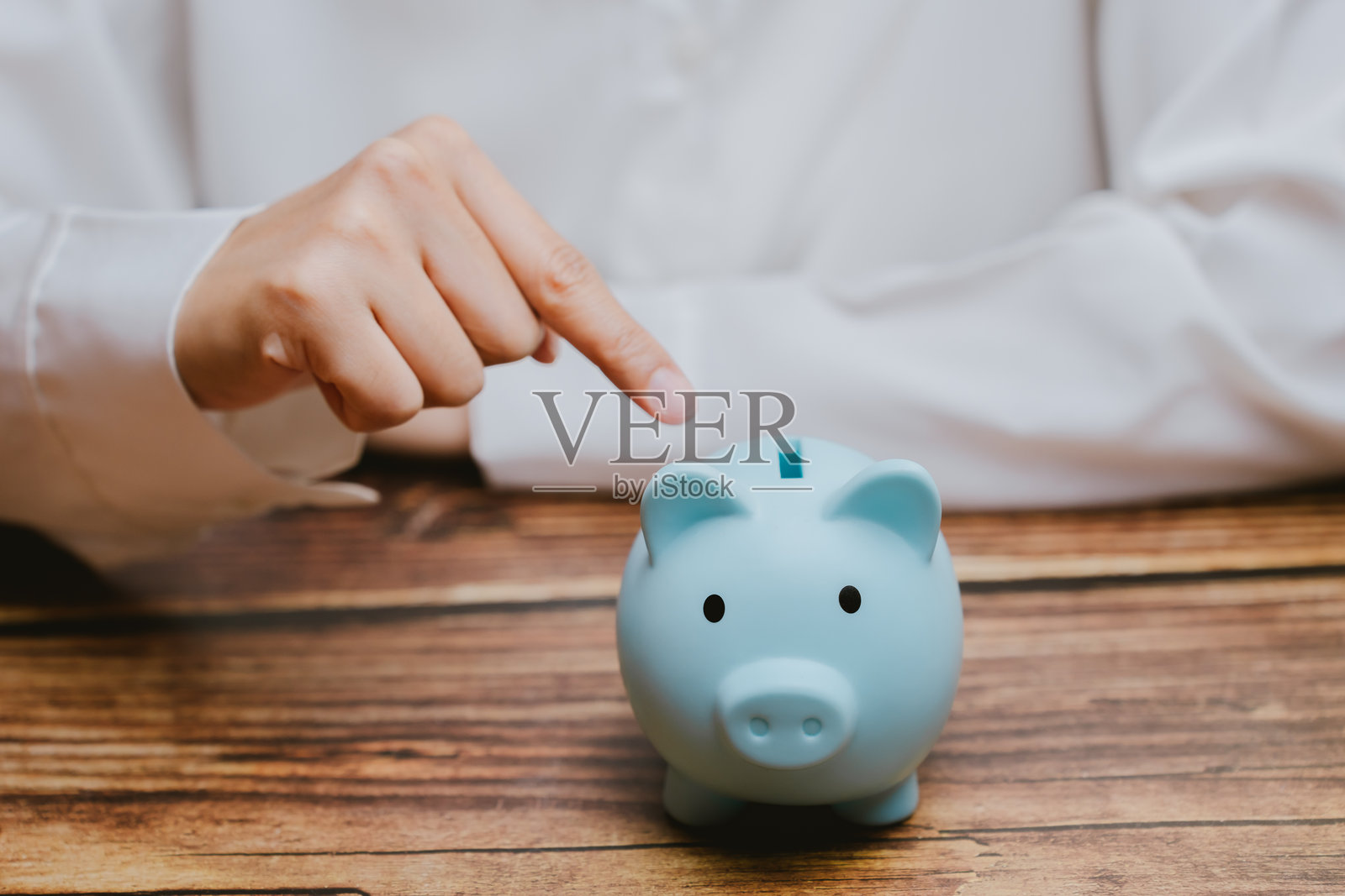 手指指向木桌上的蓝色储蓄罐，储蓄的概念照片摄影图片