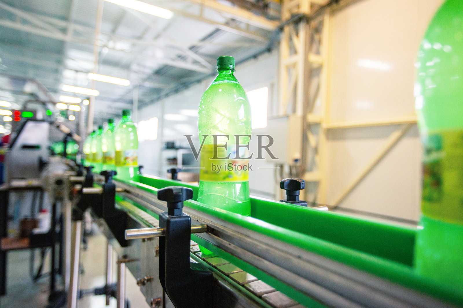 白天时，工厂的传送带上移动着绿色液体的瓶子照片摄影图片