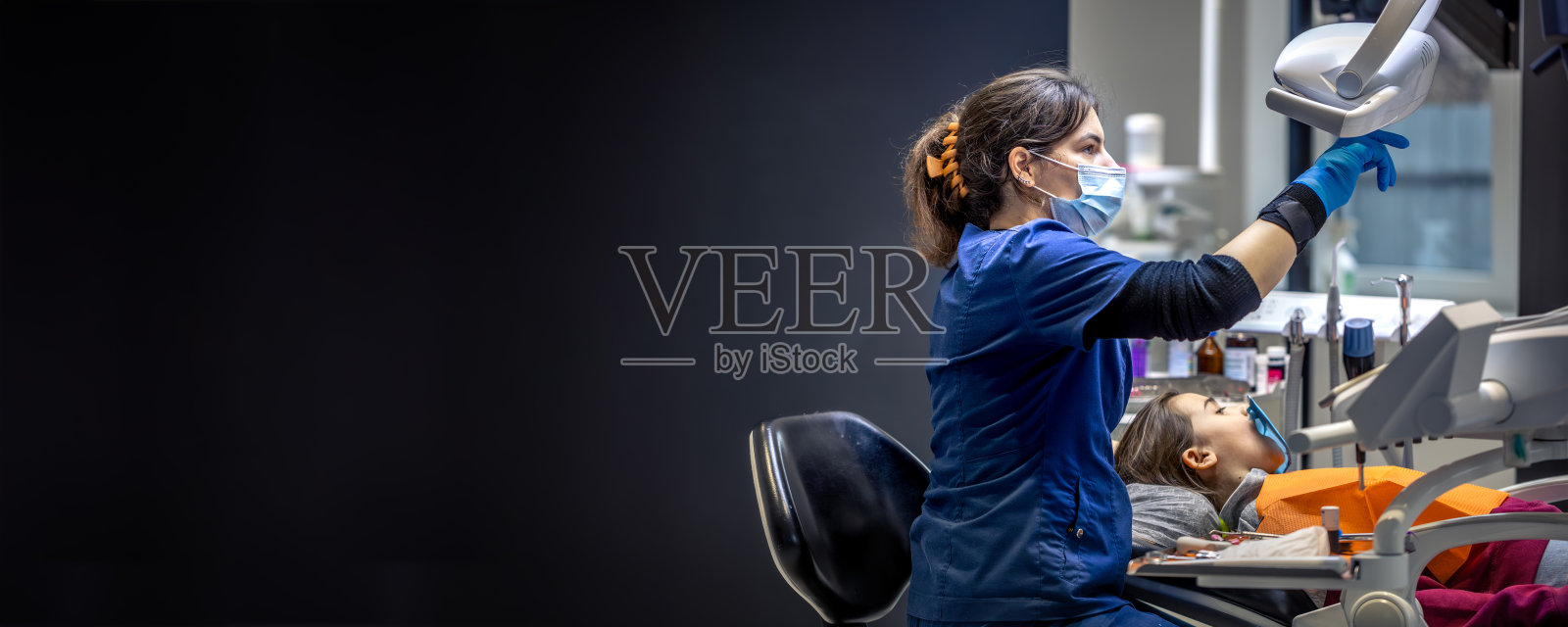 年轻女性牙医在牙科办公室为女孩治疗牙齿。牙科概念。照片摄影图片