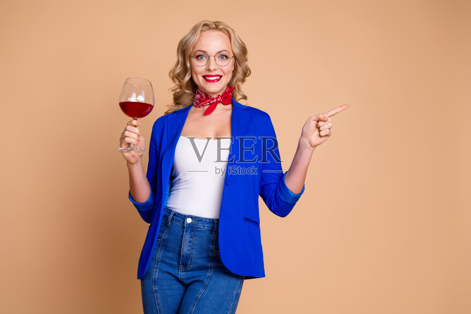 微笑的优雅女性在米色背景下手势示意，同时手中拿着一杯红酒。照片摄影图片