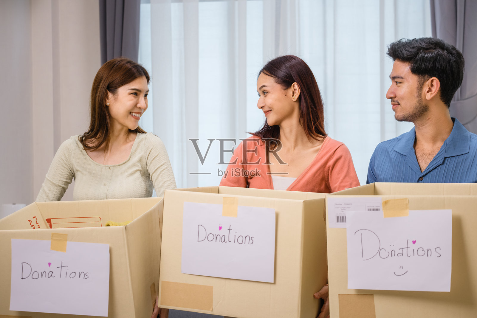 一群朋友正在整理和打包衣物放入捐赠箱，支持社区和慈善事业。照片摄影图片