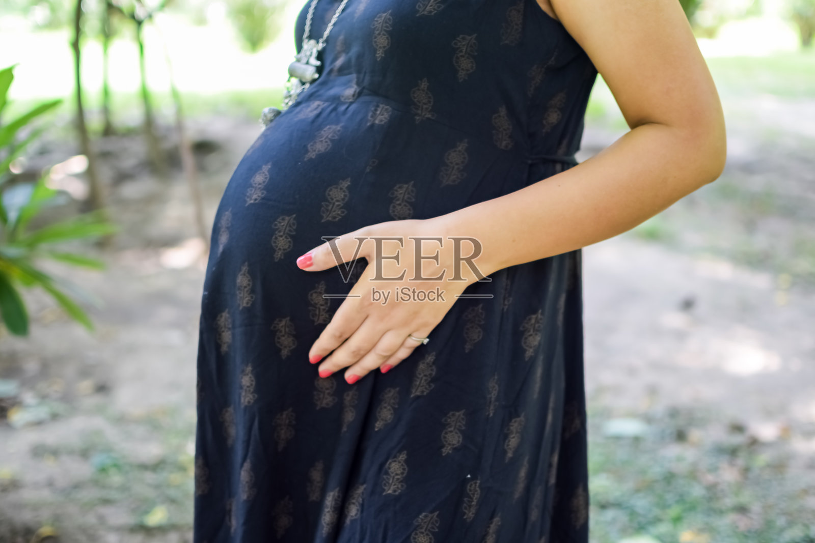 一位印度孕妇在户外拍摄孕妇照，双手放在肚子上。照片摄影图片
