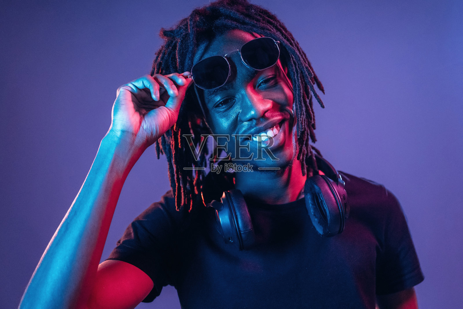 触摸太阳镜，正面视角。非裔美国男士在霓虹灯照明的摄影棚中。照片摄影图片