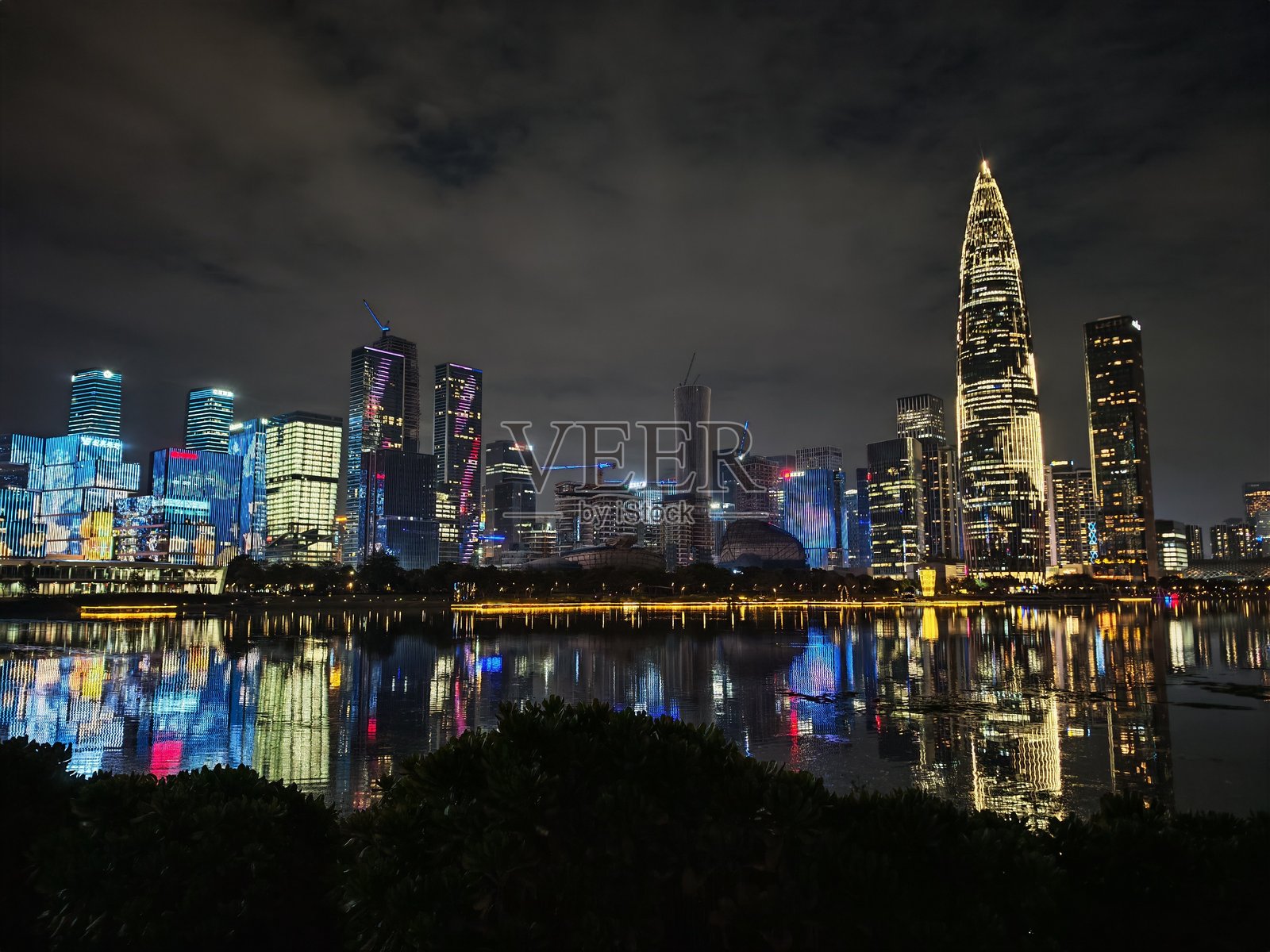 灯光照亮的建筑物勾勒出中国深圳生动的夜景,映照在黑暗夜空下的水面上。照片摄影图片