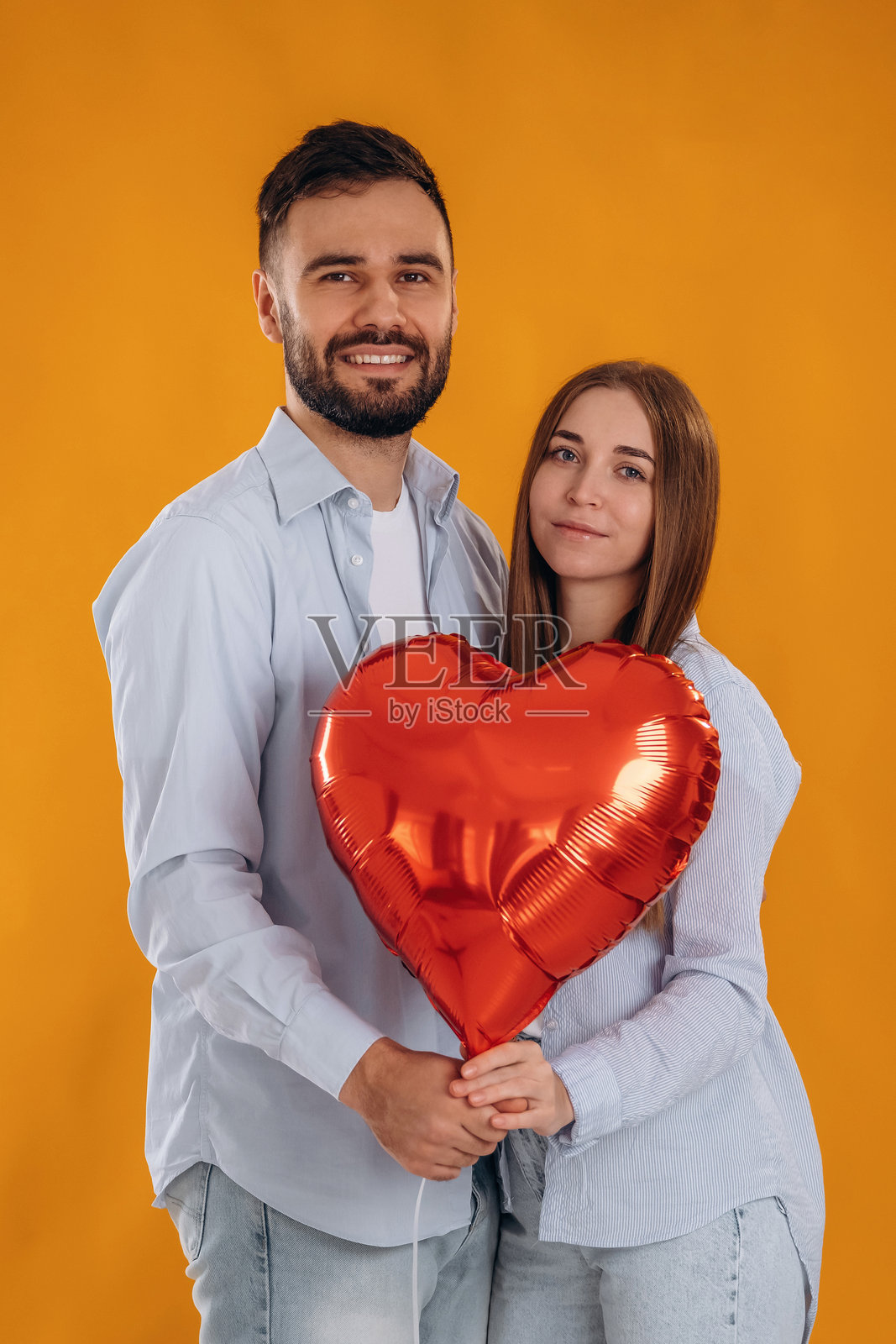 手持红色心形气球的可爱情侣在工作室里相聚照片摄影图片