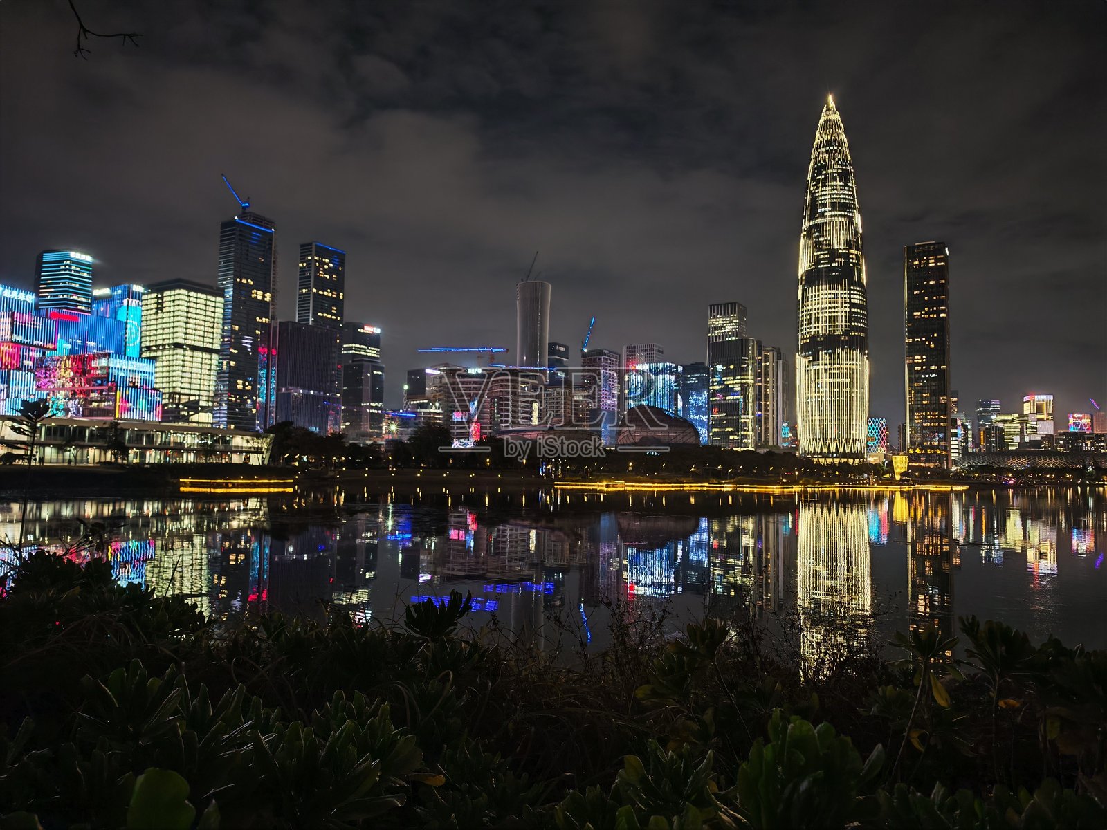 深圳,中国的夜景生动迷人,灯光闪烁的建筑在多云的天空下映照在水面上。夜晚的城市景观展现了现代都市的风貌。照片摄影图片