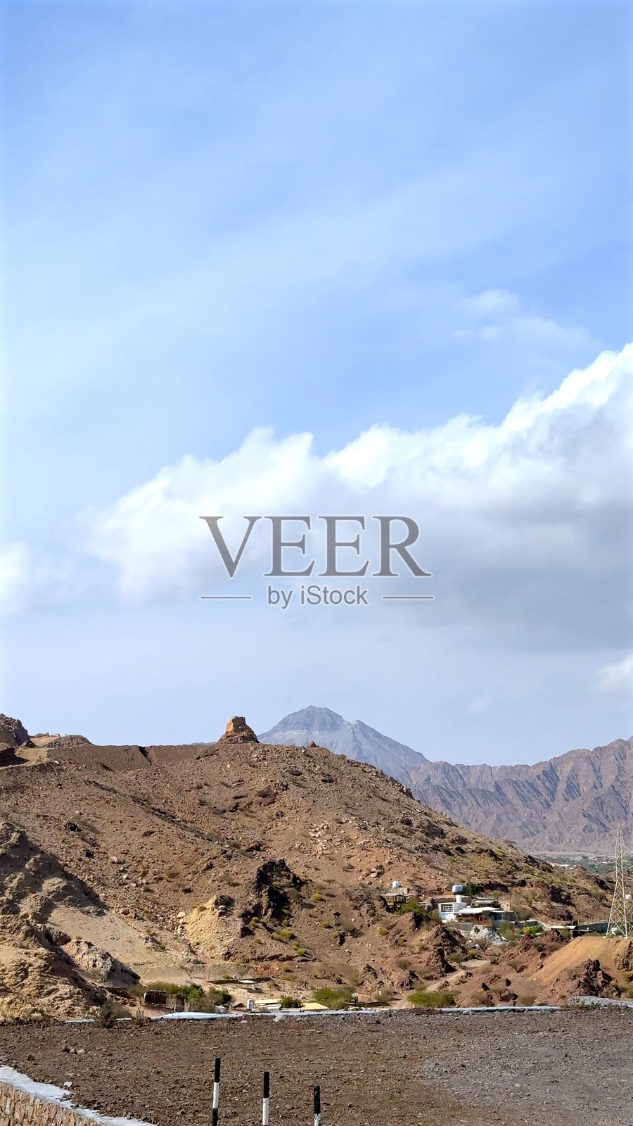 崎岖的沙漠山丘在广阔的天空下耸立，温暖的色调与蓝色的广袤形成对比，干燥的地貌被侵蚀塑造，零星的植被增添了生机，偏远的地形反映出干旱的美。照片摄影图片