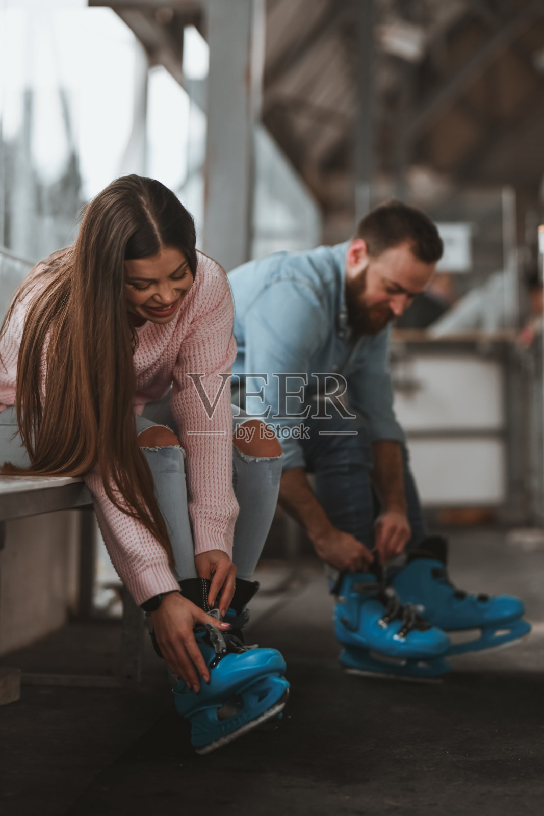 快乐的情侣坐在长椅上，默默地调整着他们的冰鞋，准备滑冰。照片摄影图片