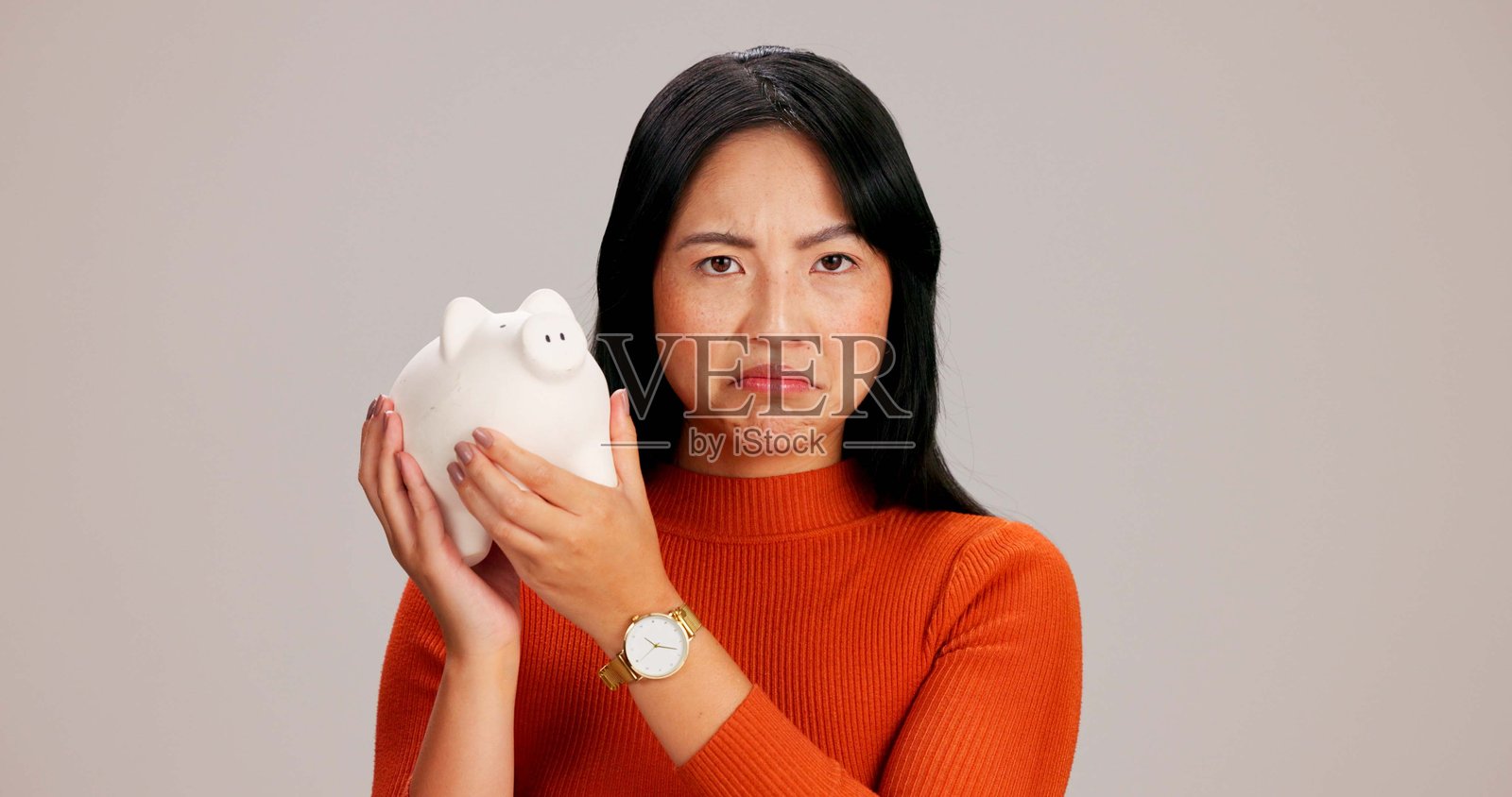 女人，悲伤的空储蓄罐在工作室肖像中，背景与储蓄、财务或预算相关。亚洲女孩，困惑或沮丧，手中拿着用于硬币、现金和财富的动物玩具容器。照片摄影图片