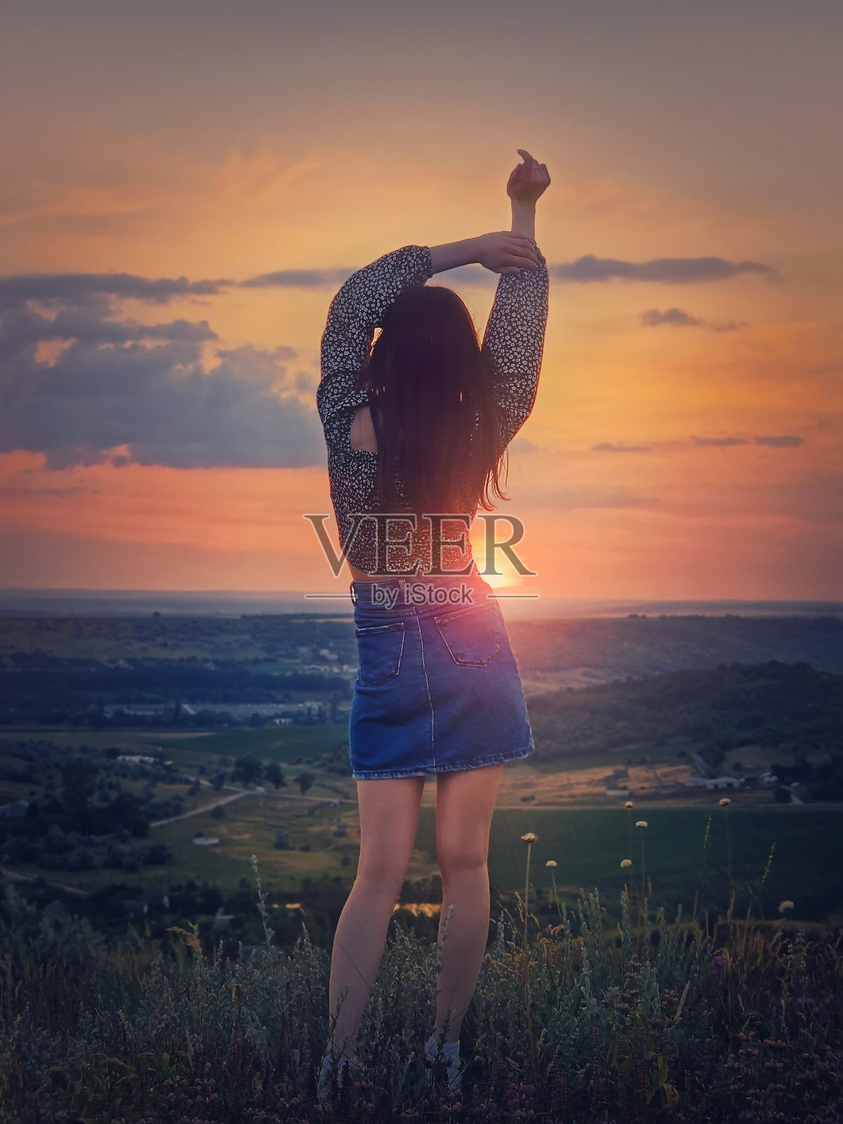 野性与自由的青春概念，一位放松的女孩背对着，双手高举在风中，面对美丽的夏季日落，站在山顶俯瞰山谷。照片摄影图片
