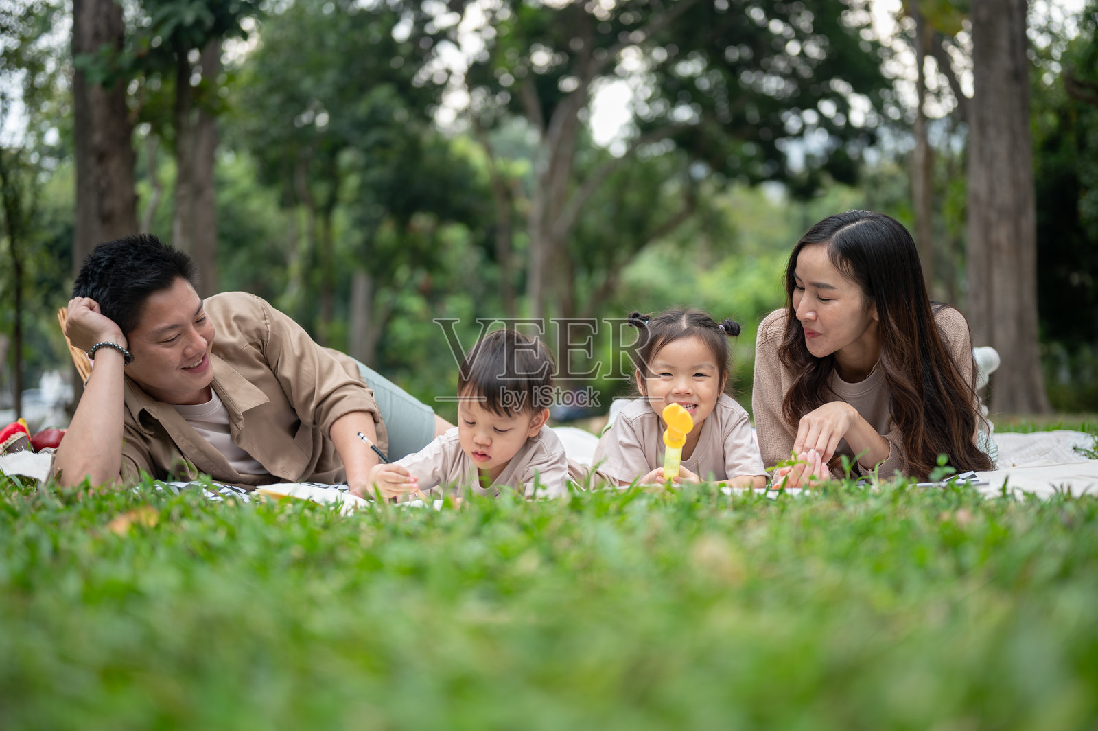 一个快乐的亚洲家庭躺在公园的野餐毯上，一起享受愉快的野餐时光。照片摄影图片