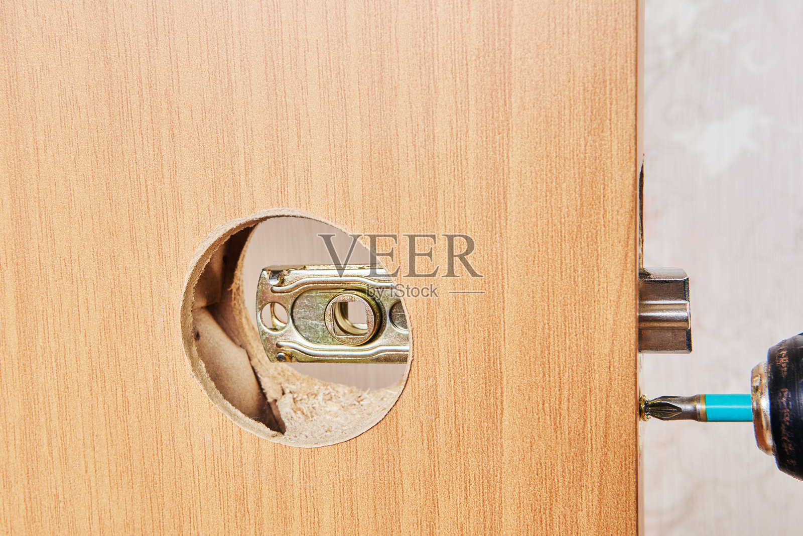 无线电钻用于将锁扣板用螺丝固定到门板上，通过圆形切口对齐。照片摄影图片